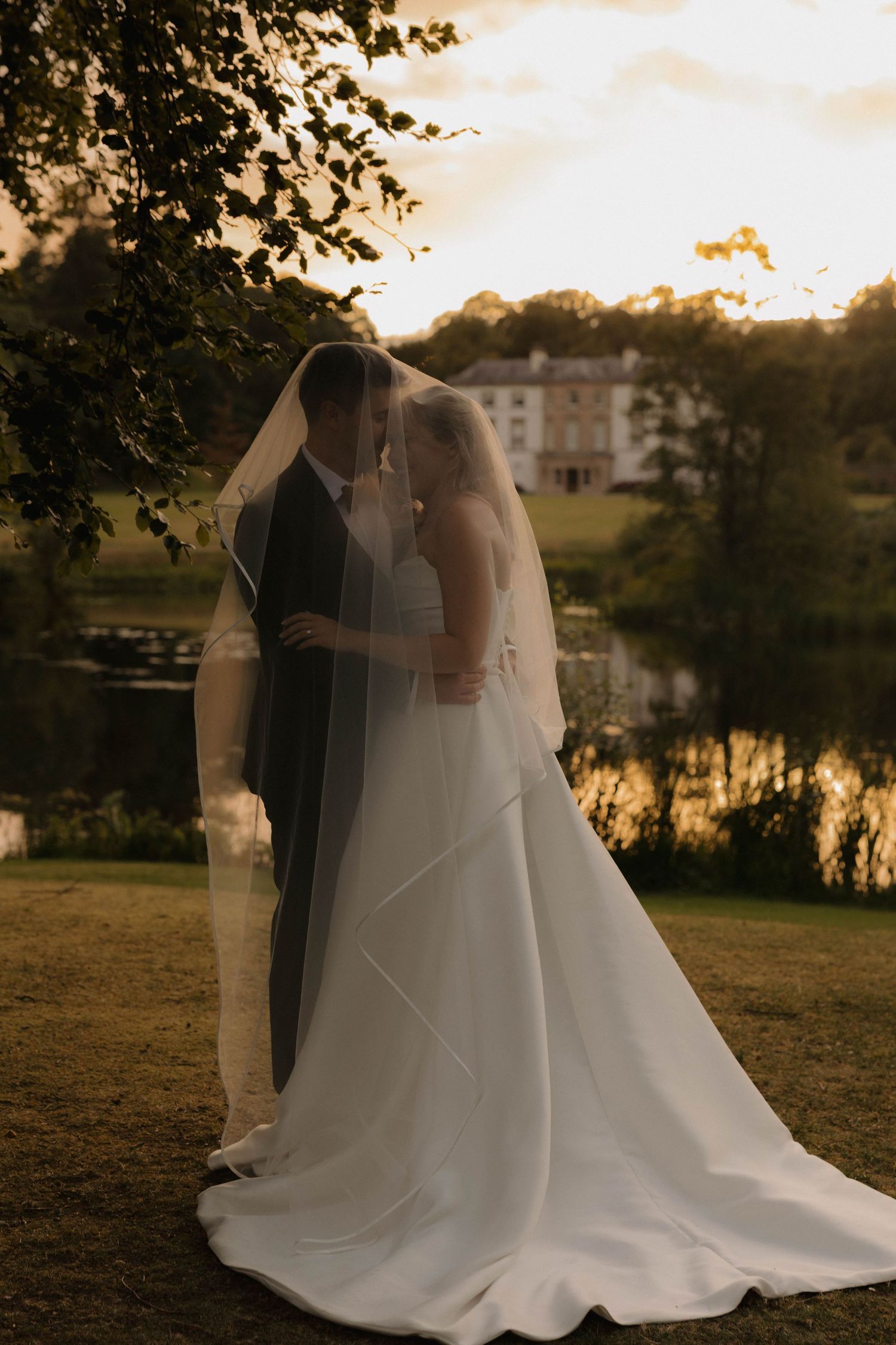 A romantic sunset wedding photoshoot featuring silhouettes of a couple in an elegant garden setting with a flowing white gown.