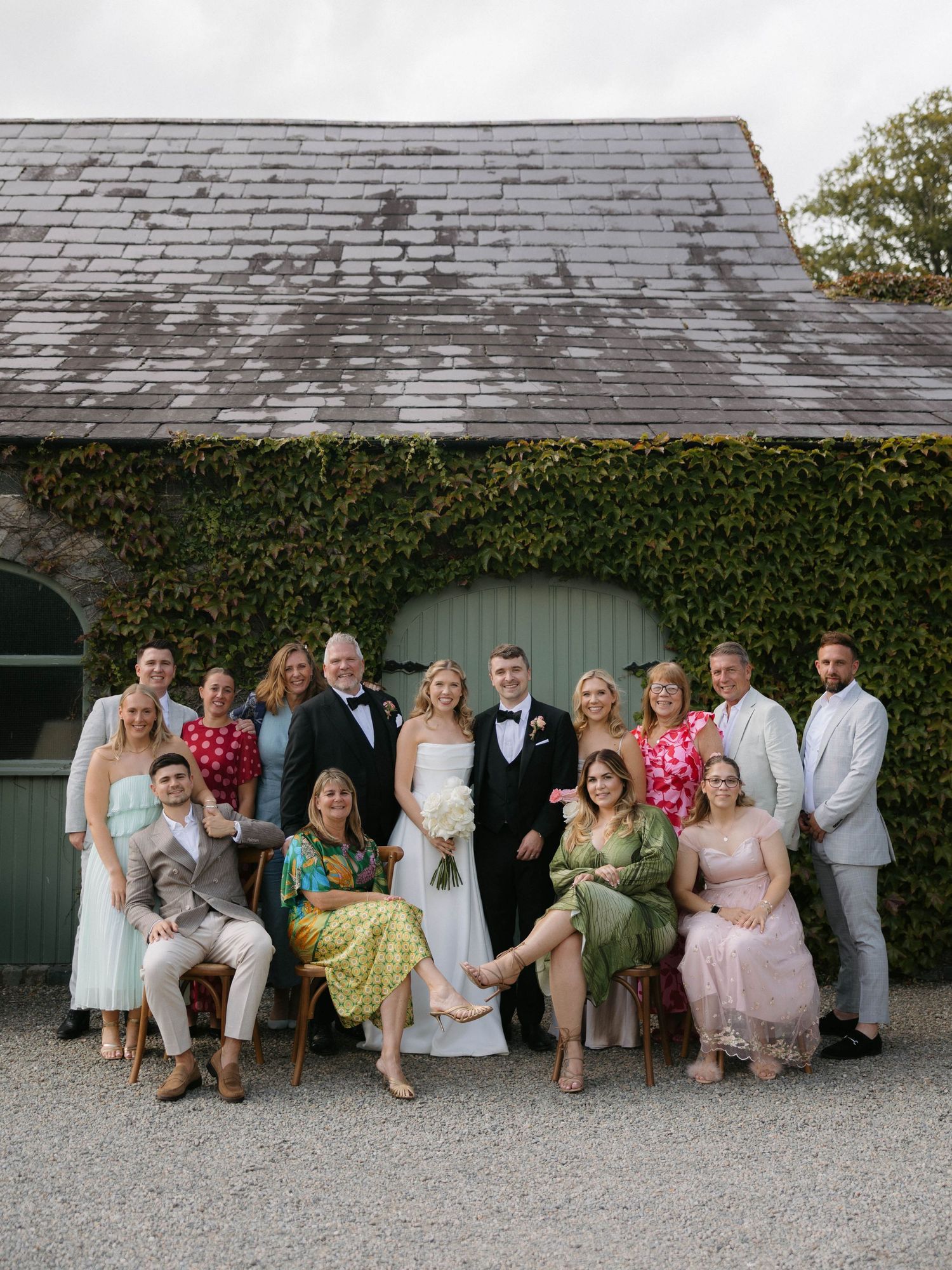 Wedding group portrait against ivy-covered building with casual summer attire.