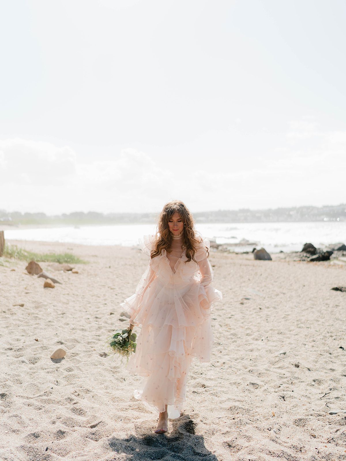 Dreamy beach bridal portrait featuring a flowy blush wedding dress and natural coastal backdrop.