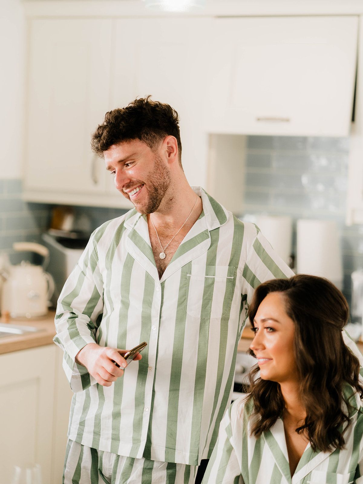 Two people wearing matching striped pajamas share a moment in bright modern kitchen.