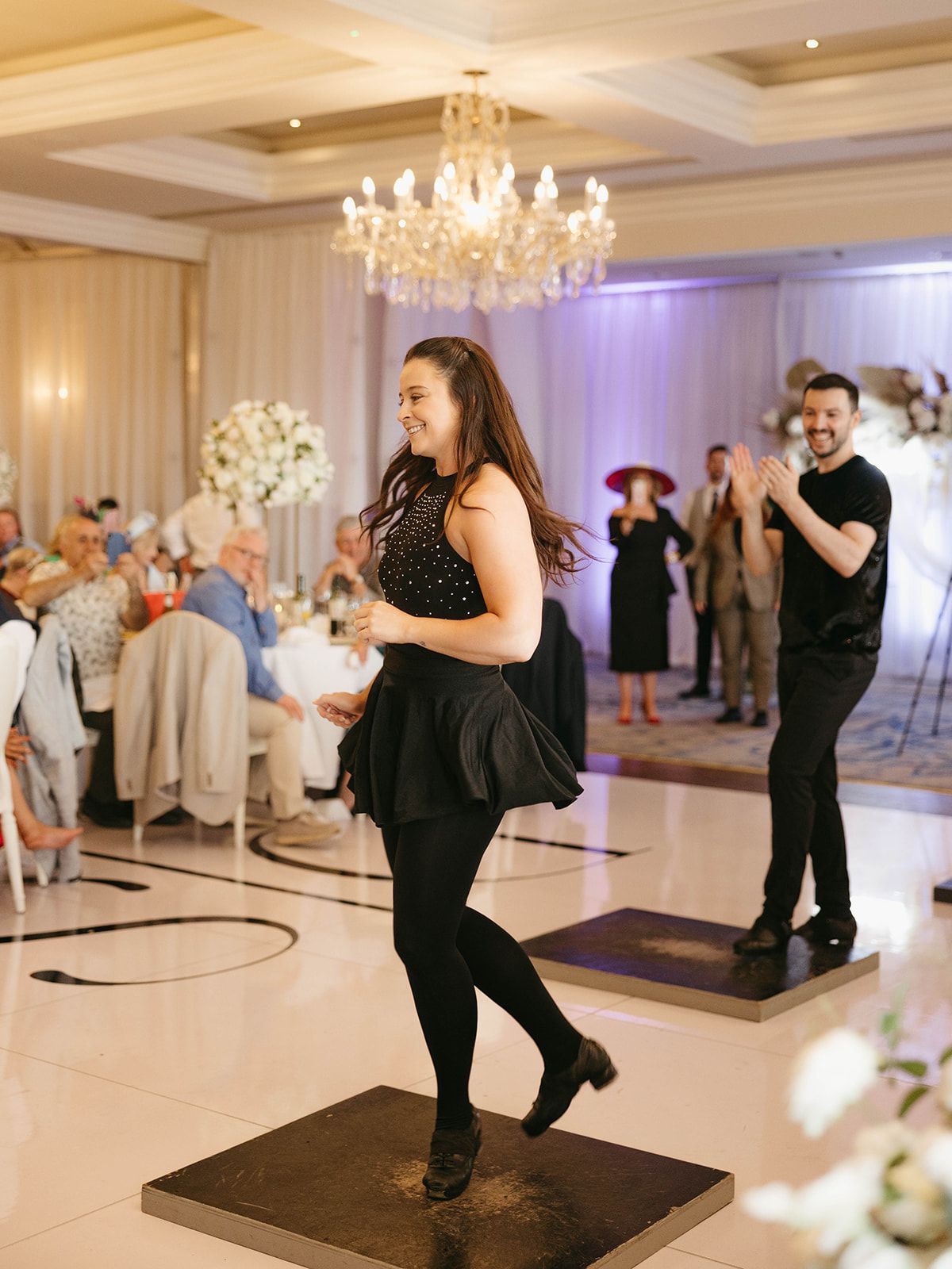 Guests dancing on wooden platforms at an elegant ballroom reception with crystal chandelier and floral decorations.