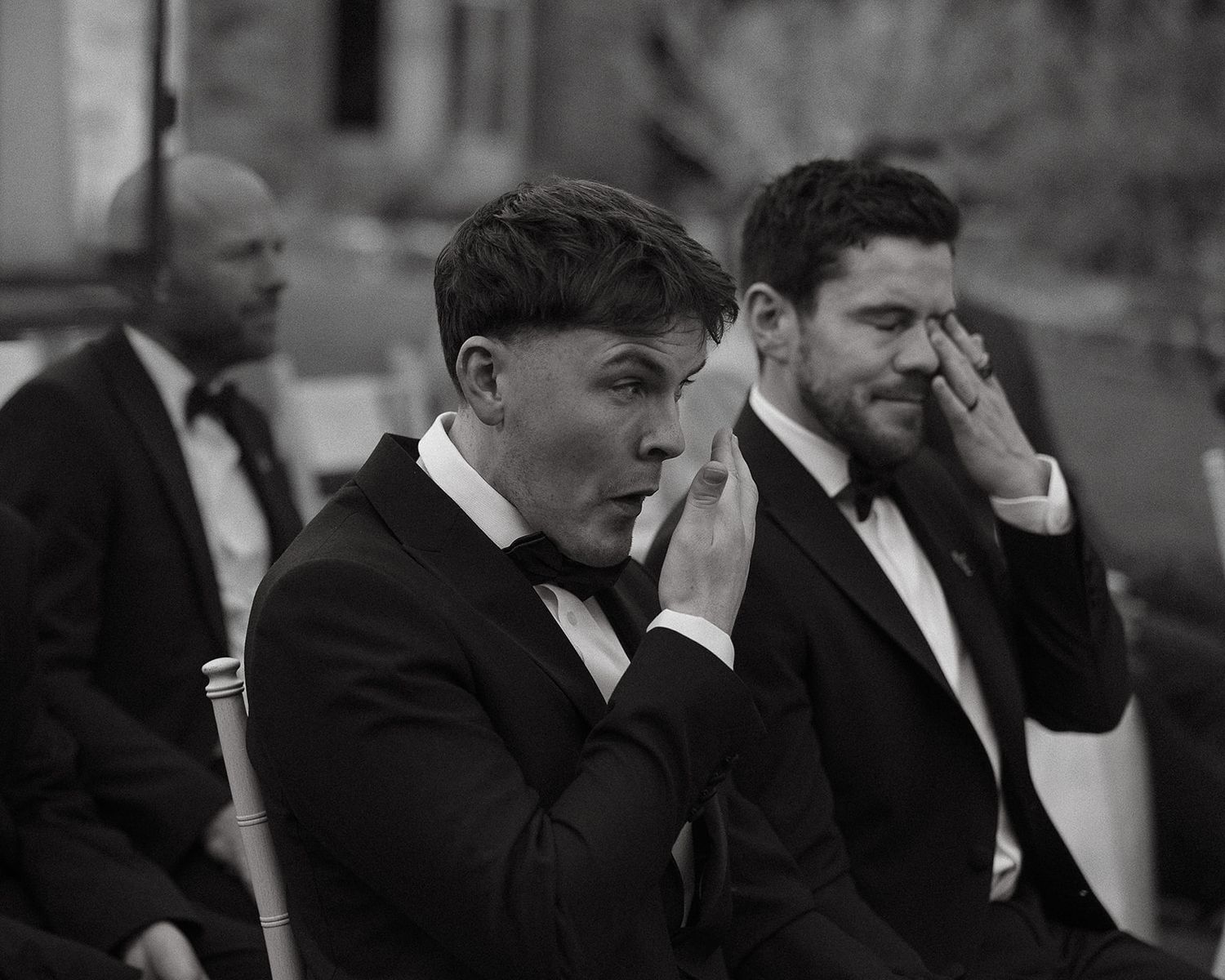 Two men in tuxedos wipe away tears during an emotional wedding ceremony.