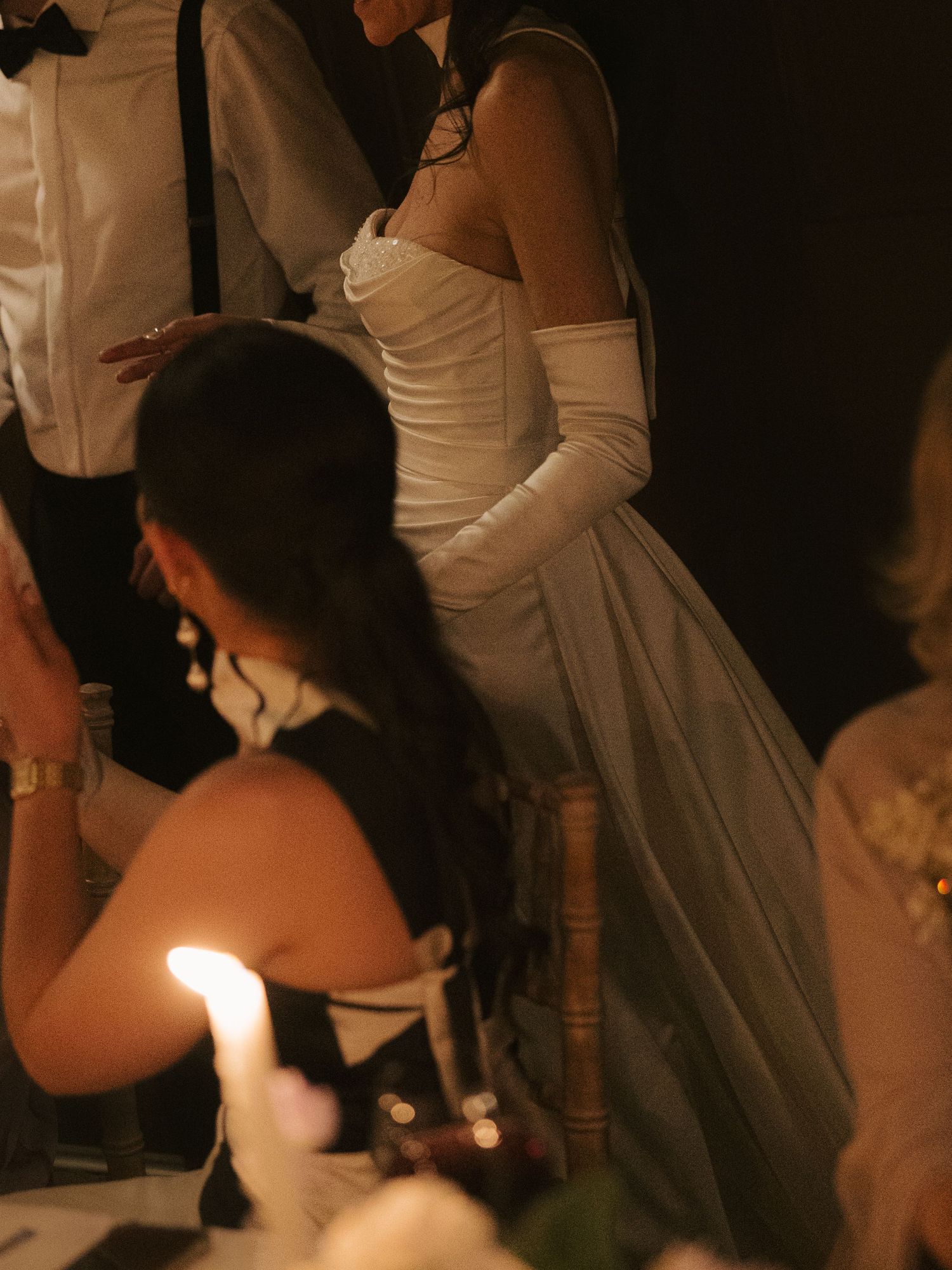 Candlelit wedding reception showing elegant white gowns and formal attire in dim lighting.