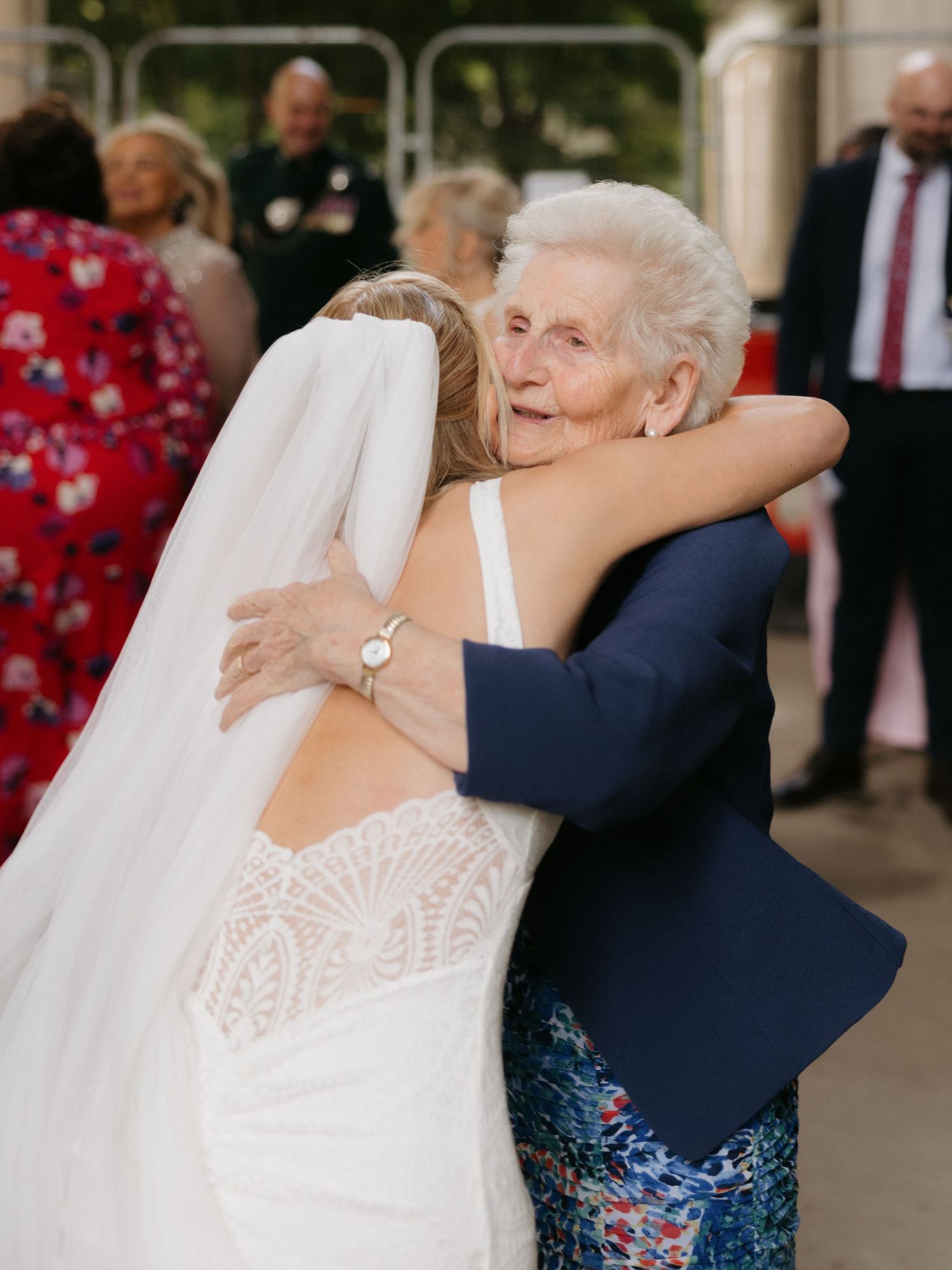 A touching moment shows a bride in white embracing someone wearing blue floral attire at a wedding celebration.