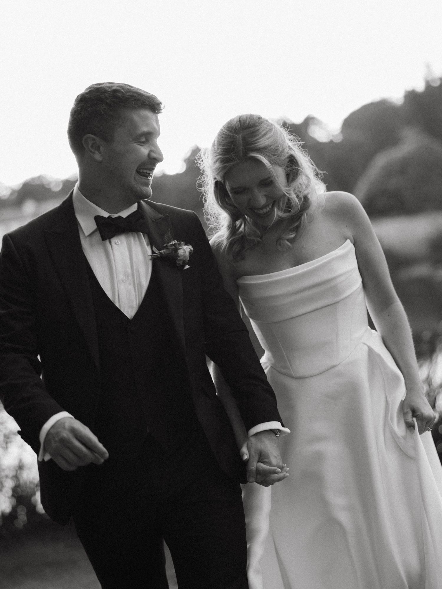Black and white portrait of a couple in formal wedding attire walking together outdoors.