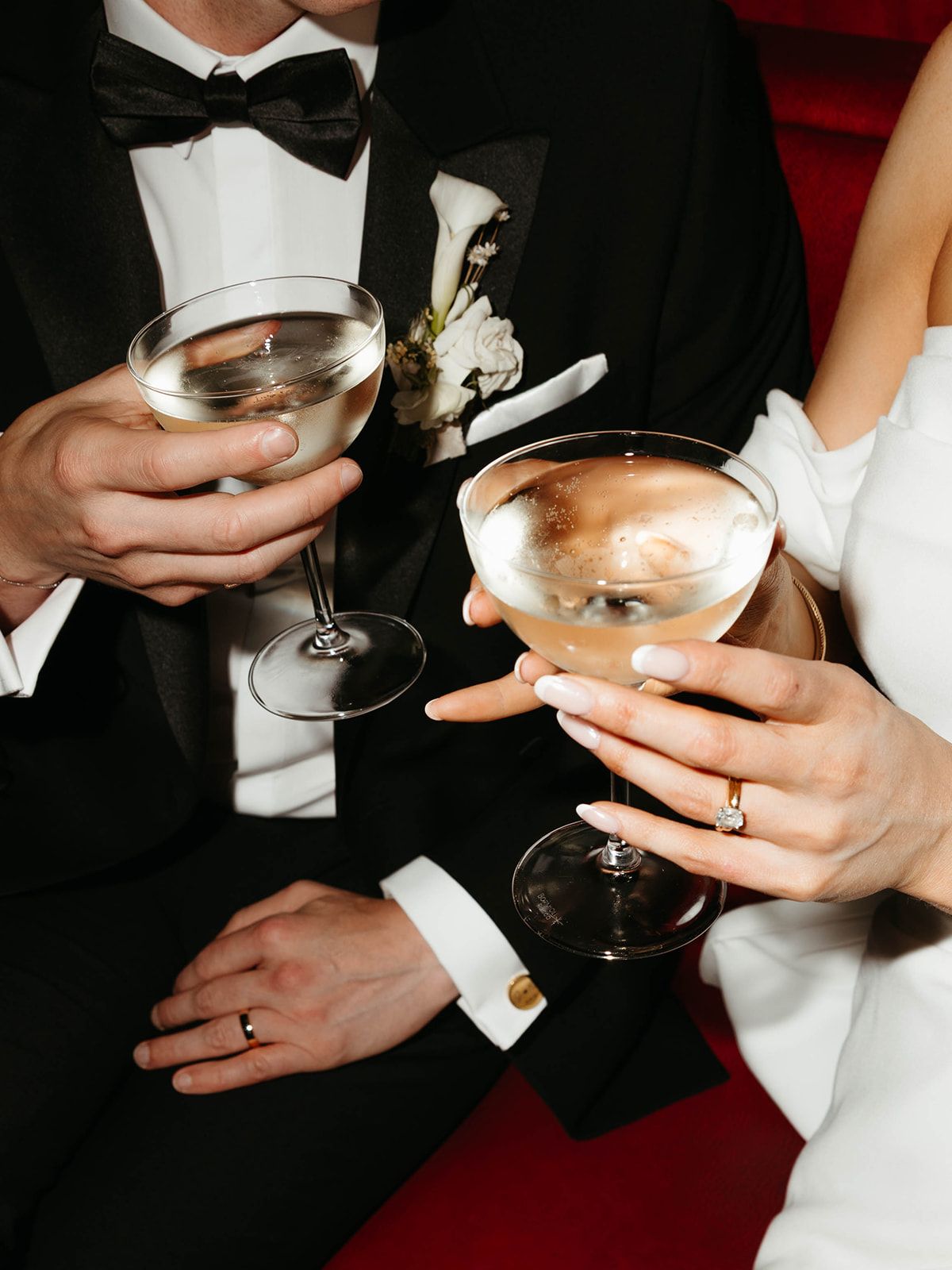 Hands holding champagne glasses with a wedding ring visible during a formal celebration.