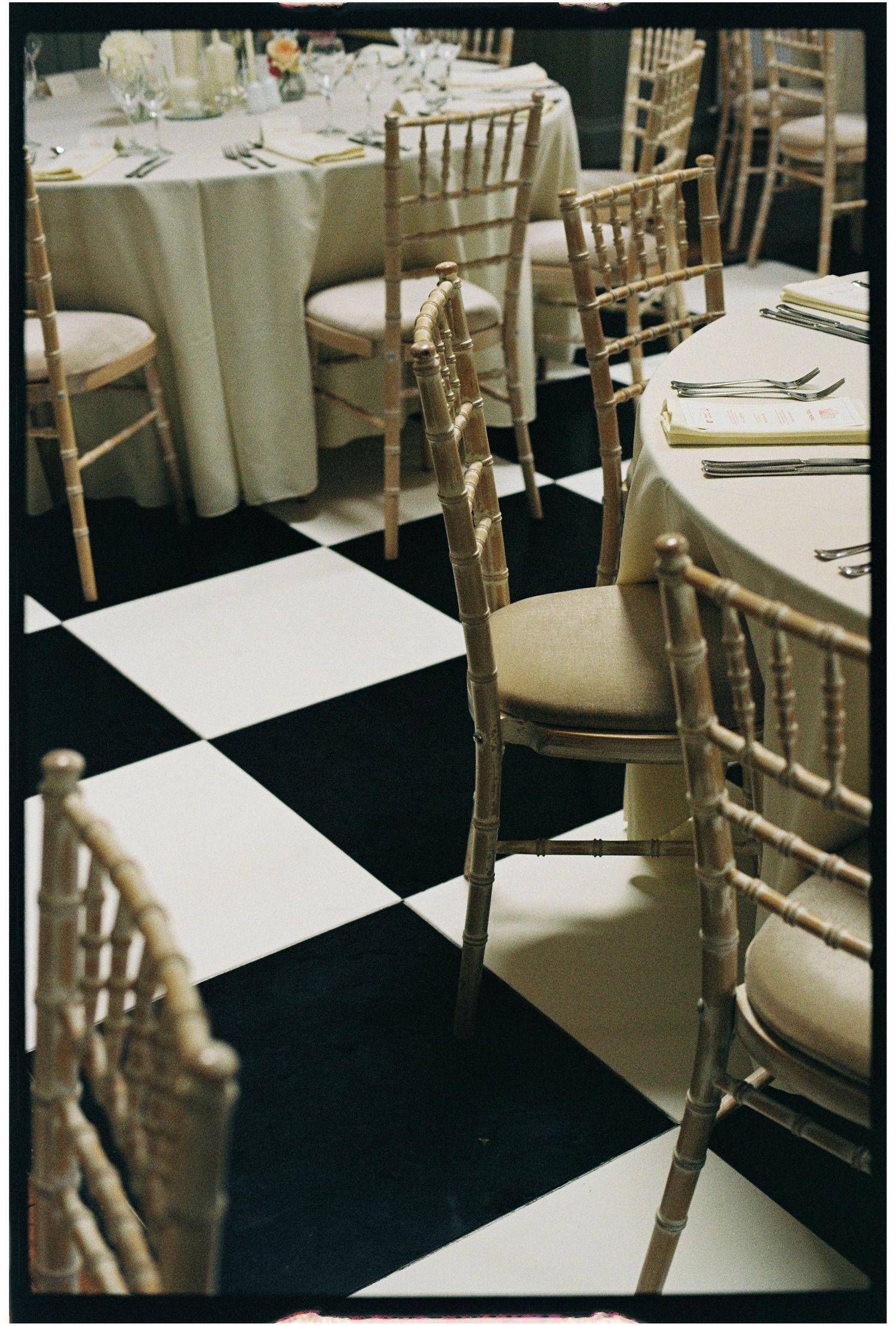 Gold chiavari chairs arranged around white linen tables on black and white checkered floor.