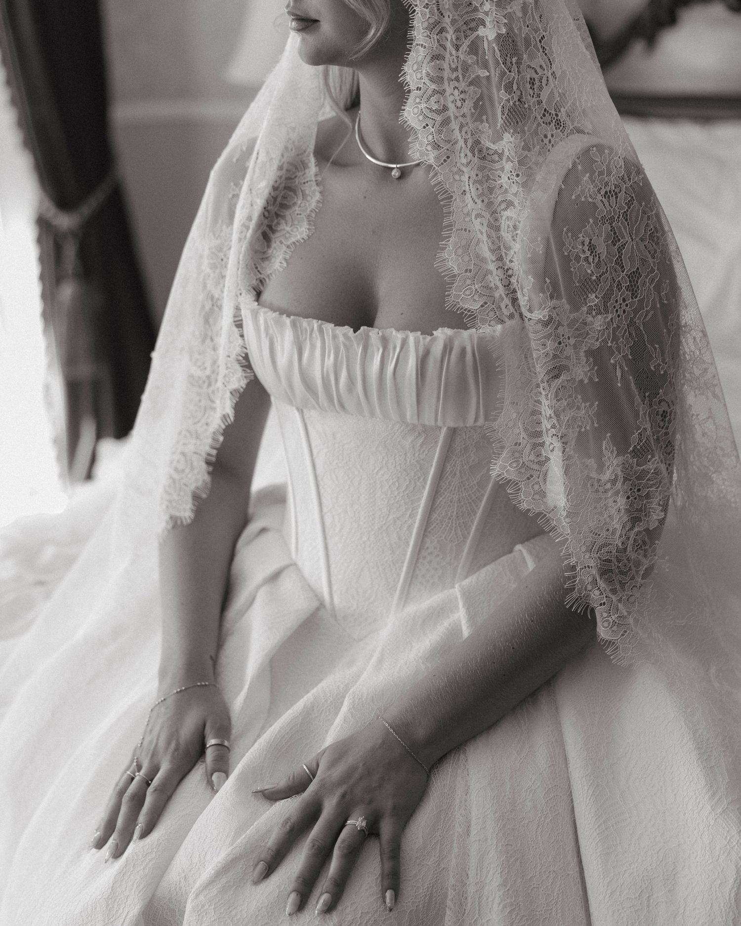 Elegant bride in a white corset wedding gown with lace veil, black and white photo.