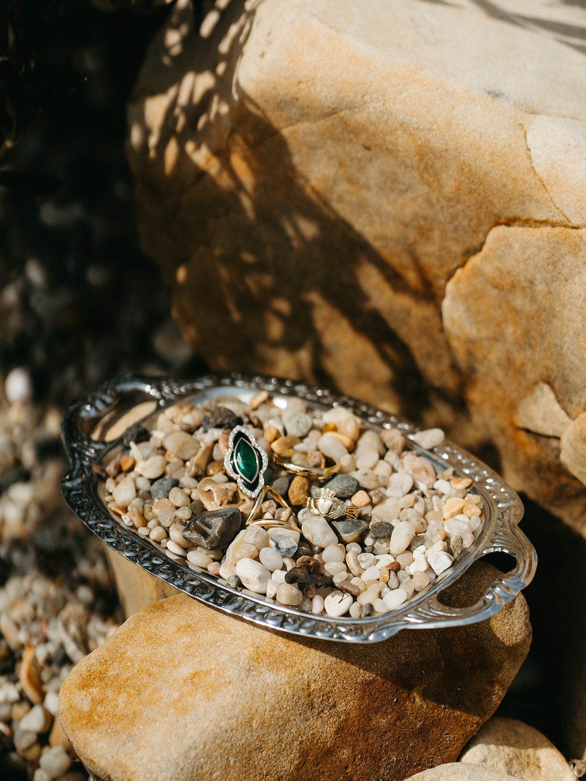 Vintage silver tray filled with small stones and a teal ring displayed on textured rock surface.
