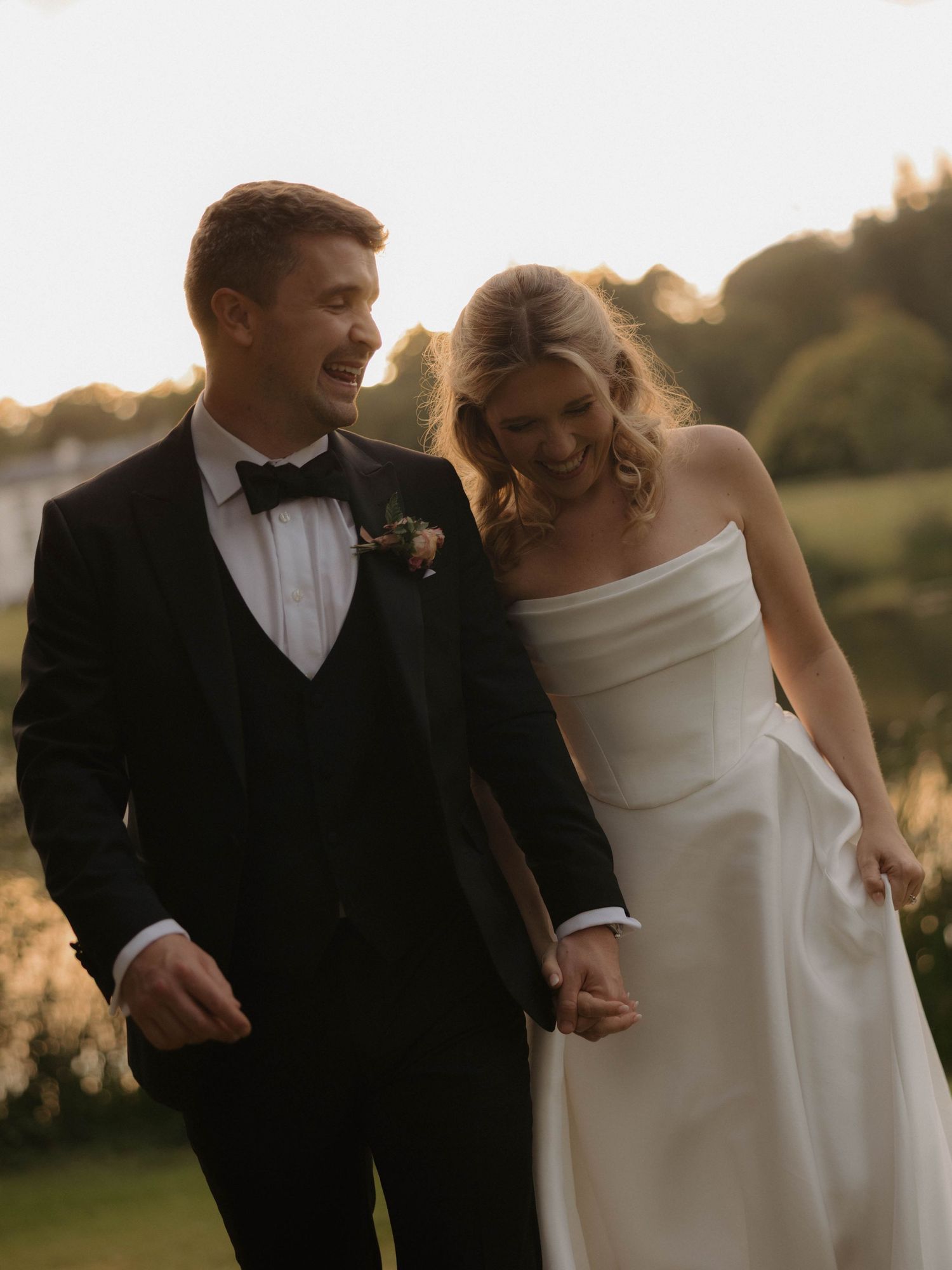 A couple shares a joyful moment together outdoors during golden hour in formal wedding attire.