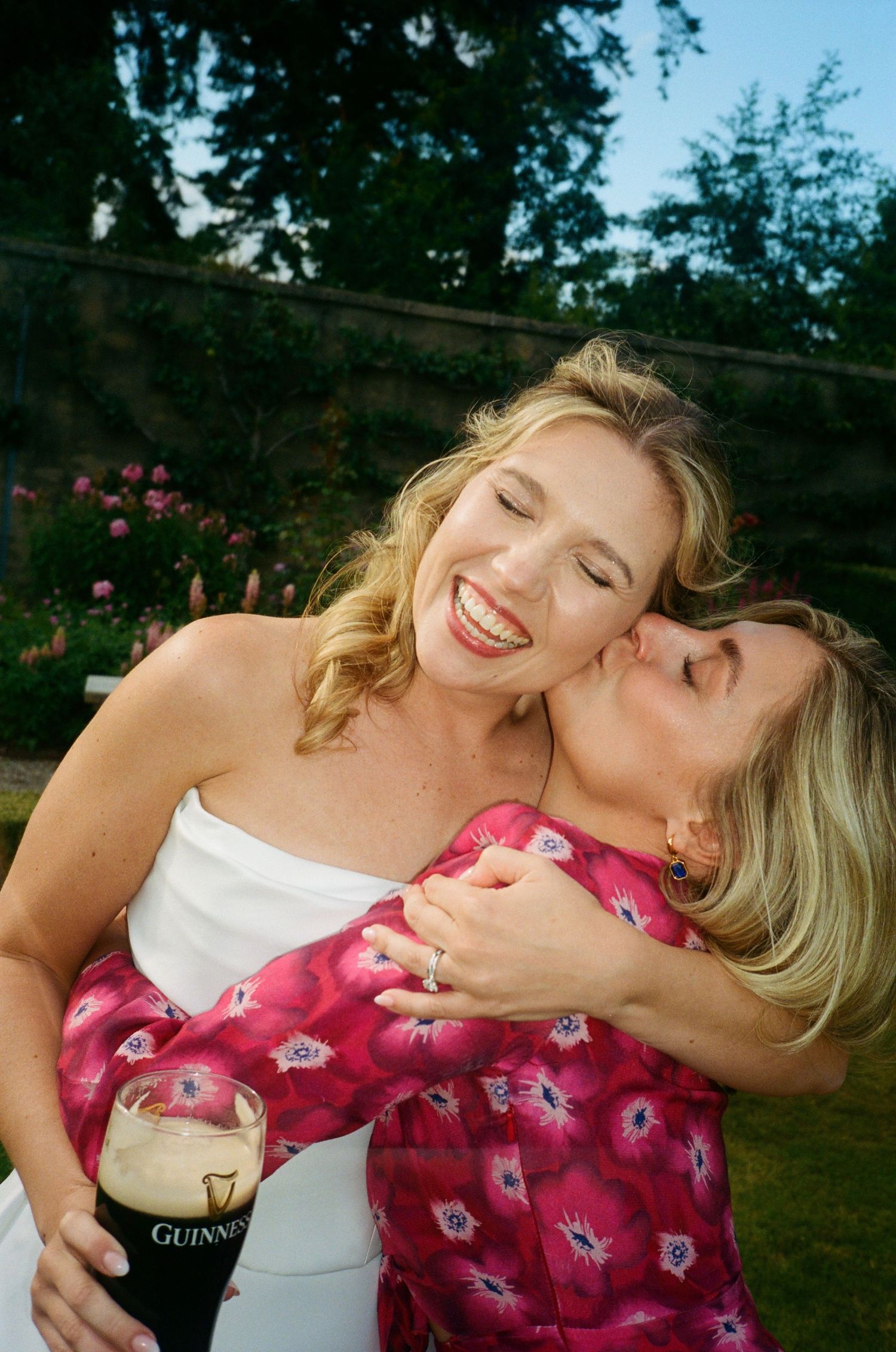Two people in white and pink floral clothing share a joyful moment together outdoors on a sunny day.