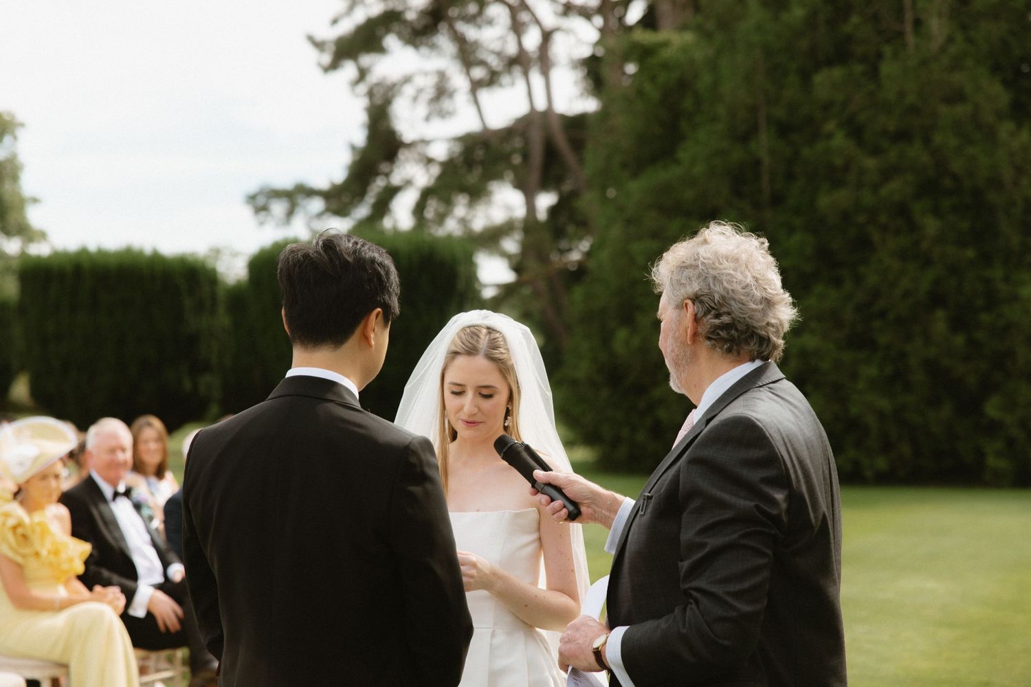 Outdoor wedding ceremony with officiant conducting vows on a sunny day.