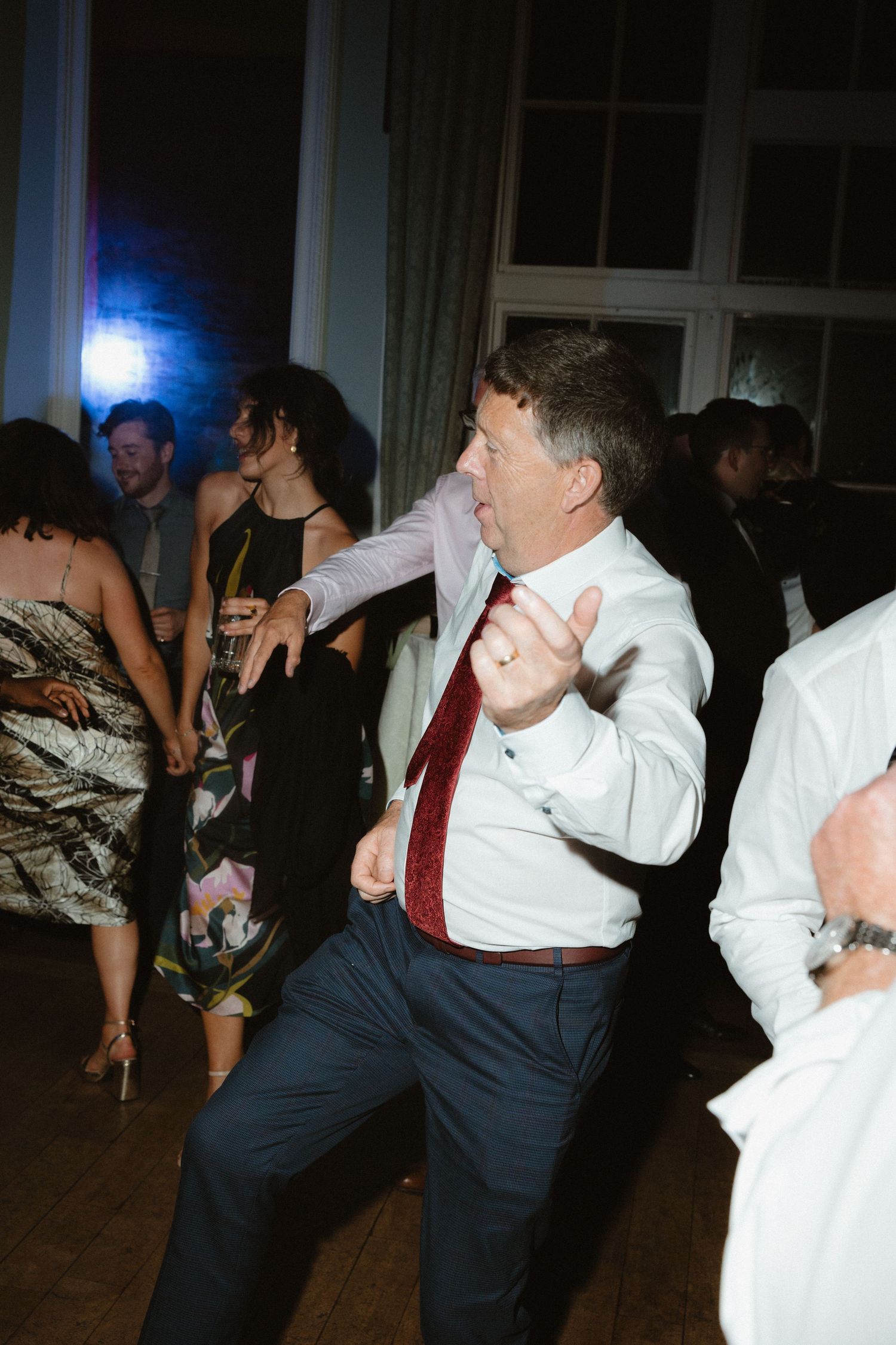 A guest in white shirt and red tie dances energetically at the wedding reception.