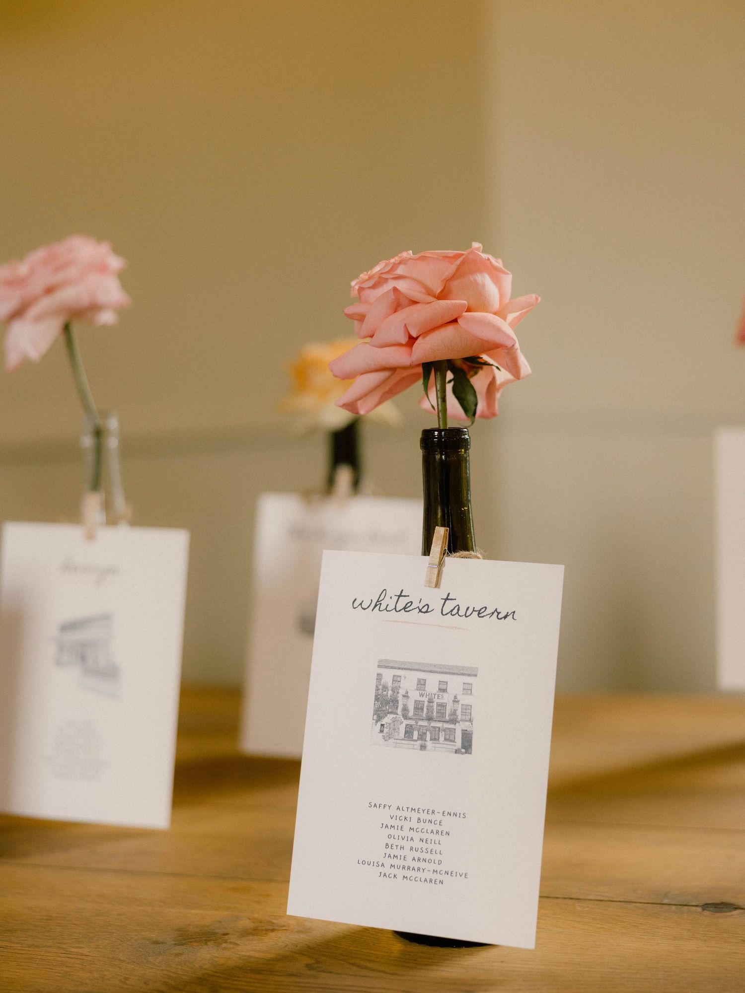 Wedding reception place cards with delicate pink flowers on a wooden table.