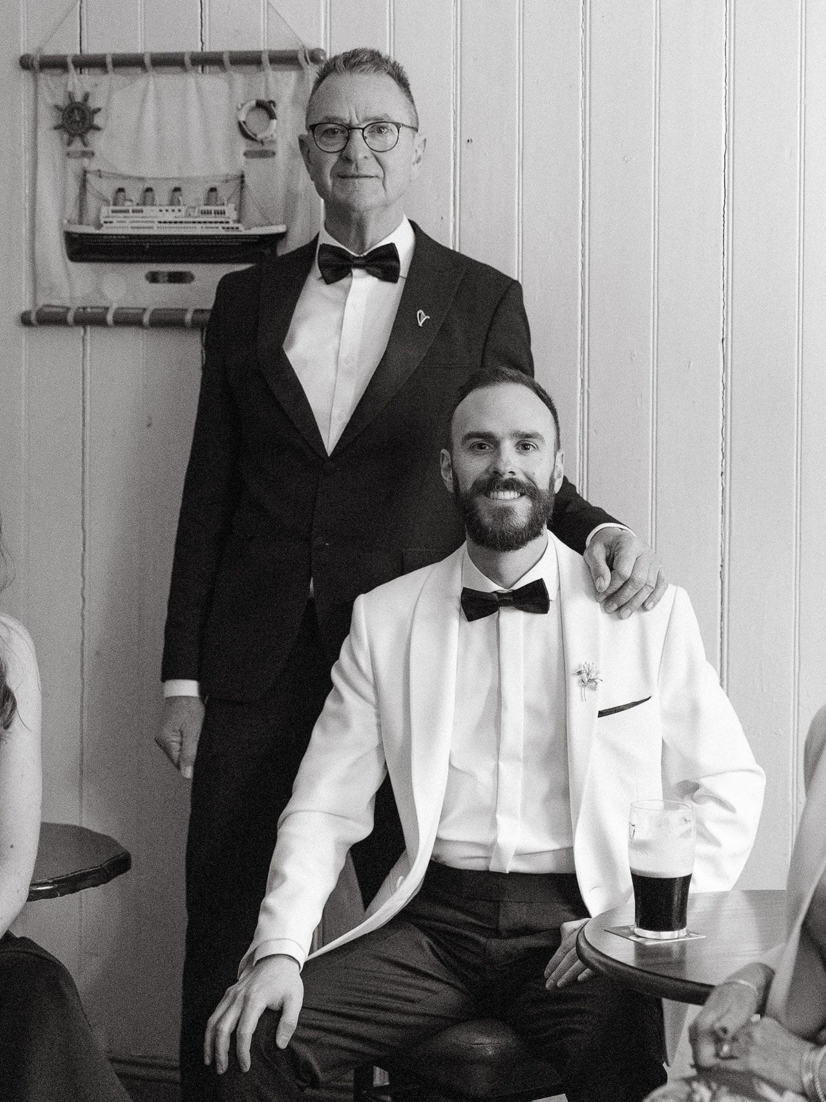 A row of men in formal black and white tuxedos and bow ties posing together in a classic wedding party style.