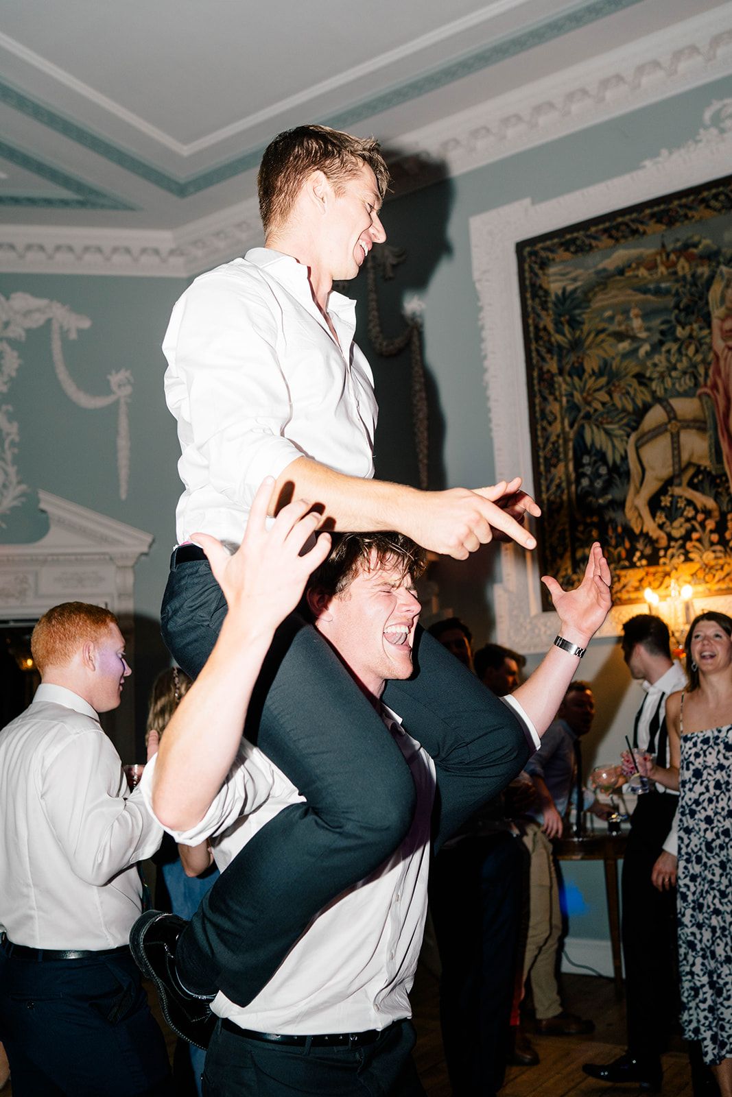 Two party guests at a wedding reception having fun with one being lifted on the other's shoulders during celebrations.