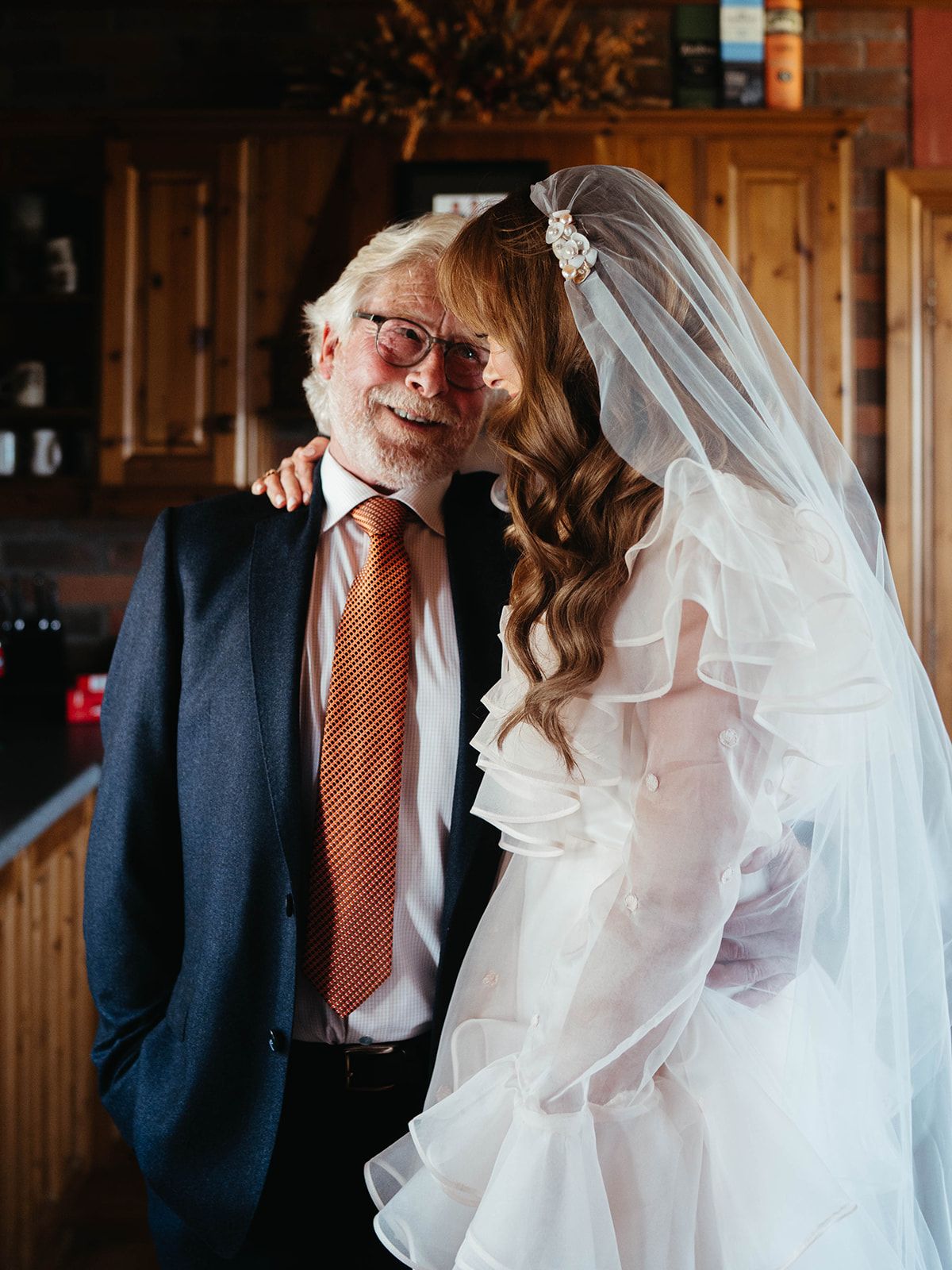 A heartwarming wedding day moment captured in a wooden-paneled kitchen setting.