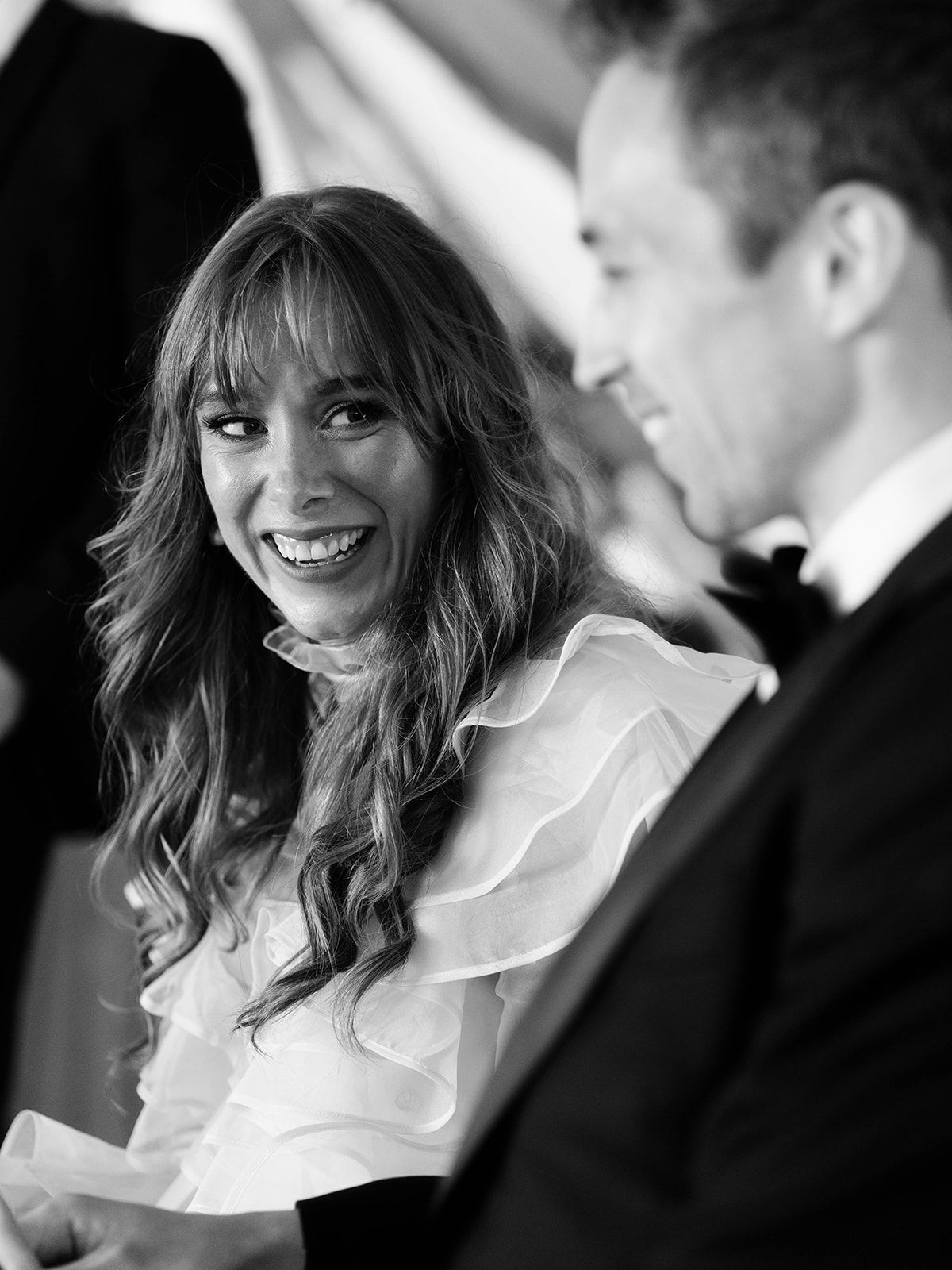 Black and white photo of bride in ruffled dress sharing emotional moment during wedding speech.
