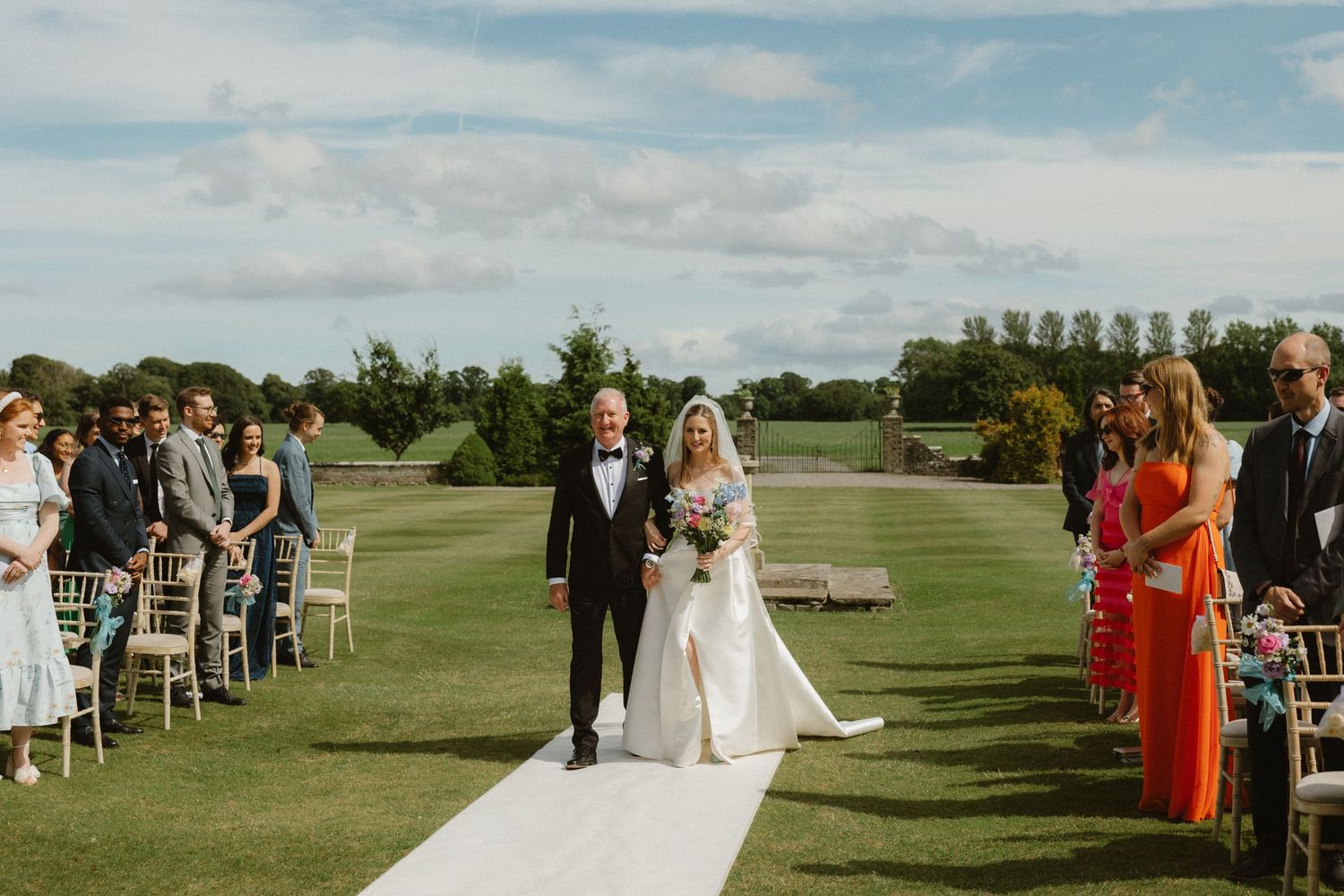 An outdoor wedding ceremony on a pristine golf course with white chairs and guests in formal attire.