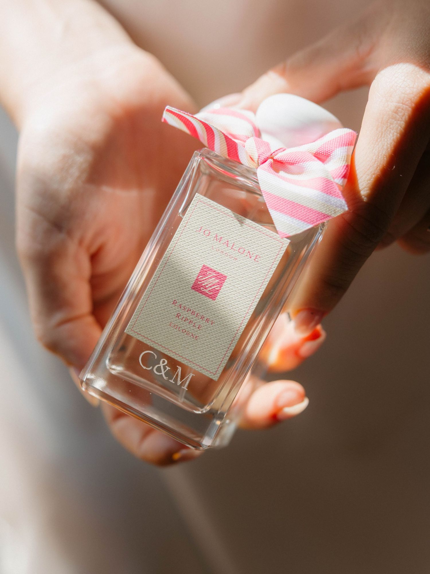 Close-up of hands holding a pink-ribboned perfume bottle with custom wedding initials.
