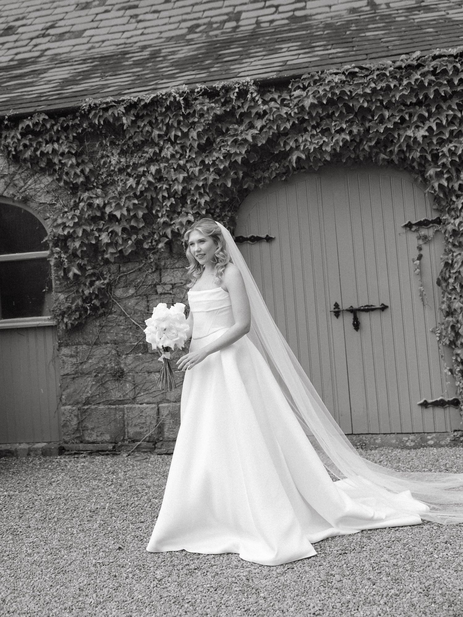 Classic black and white bridal portrait with ivy-covered walls and elegant wedding gown.