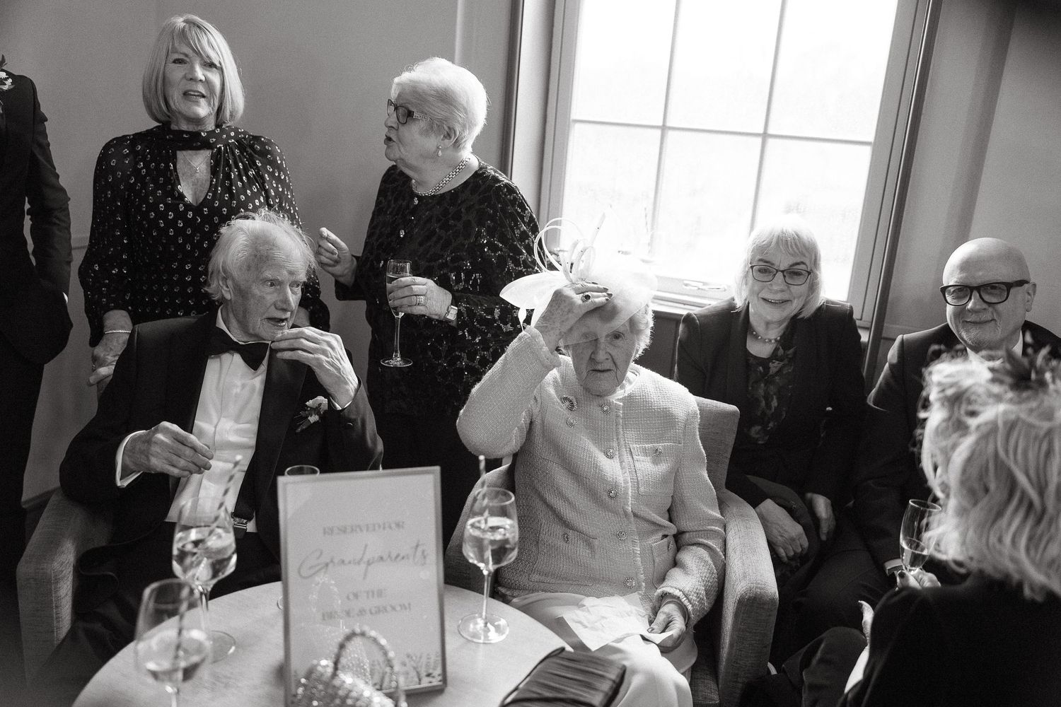 A series of black and white photos showing people gathered around tables enjoying wine and conversation at a social event.