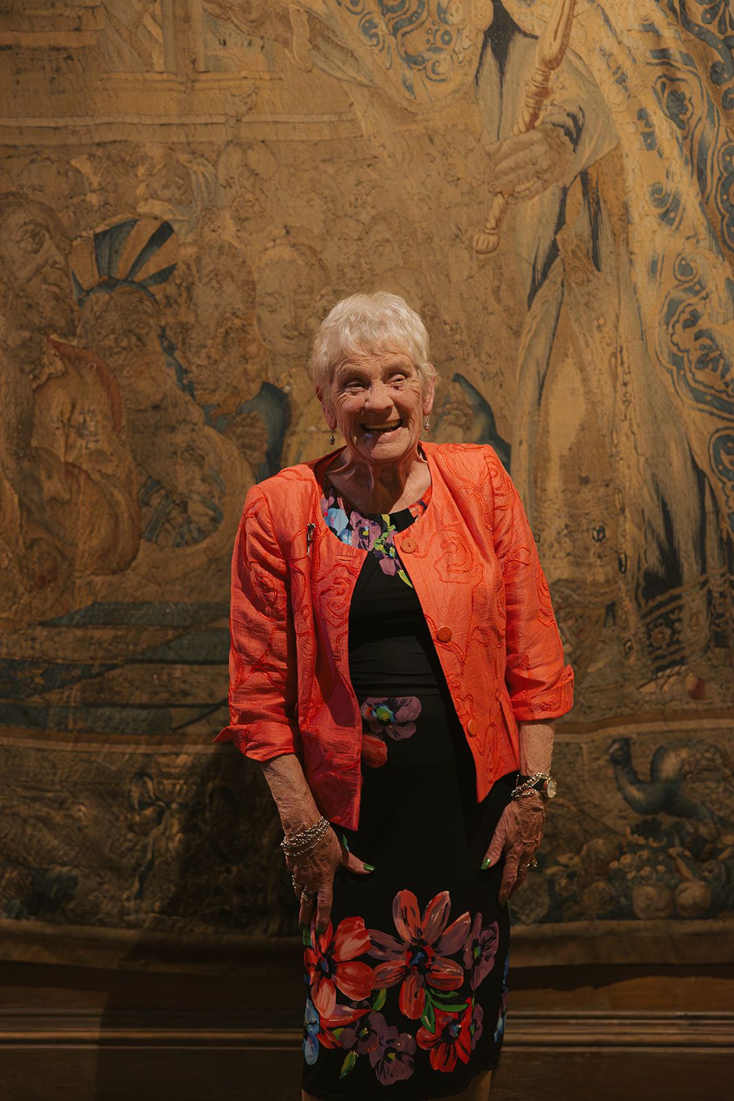 A person in a bright orange jacket poses against an ornate tapestry background in multiple artistic shots.