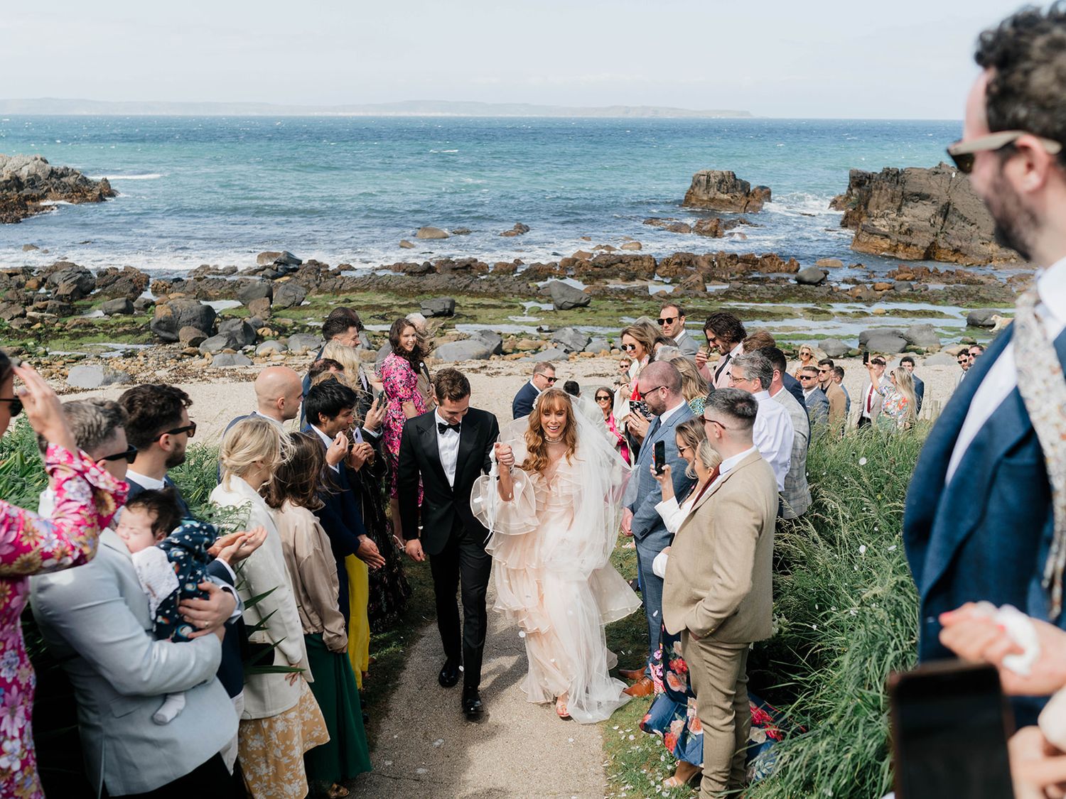 Wedding party and guests gathered on scenic coastal path for celebration.
