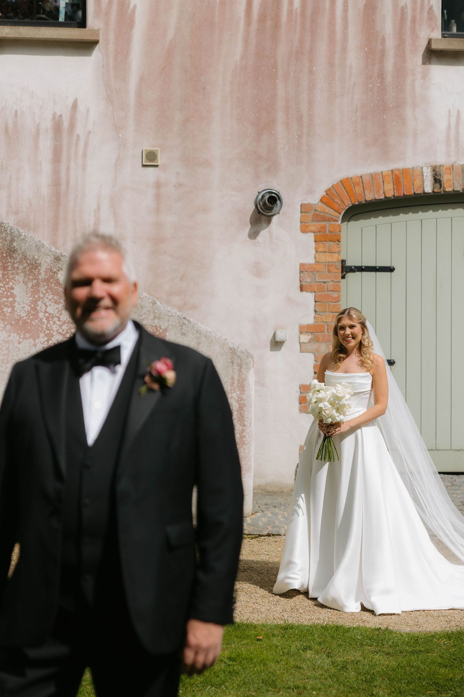 A wedding portrait in front of a rustic building with pink walls and a sage green door.