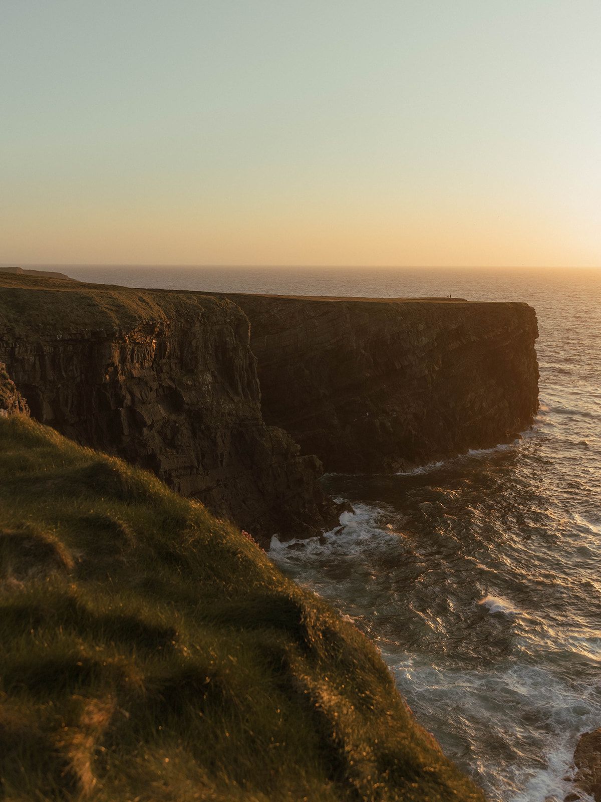 Dramatic coastal cliffs meet crashing waves at sunset.