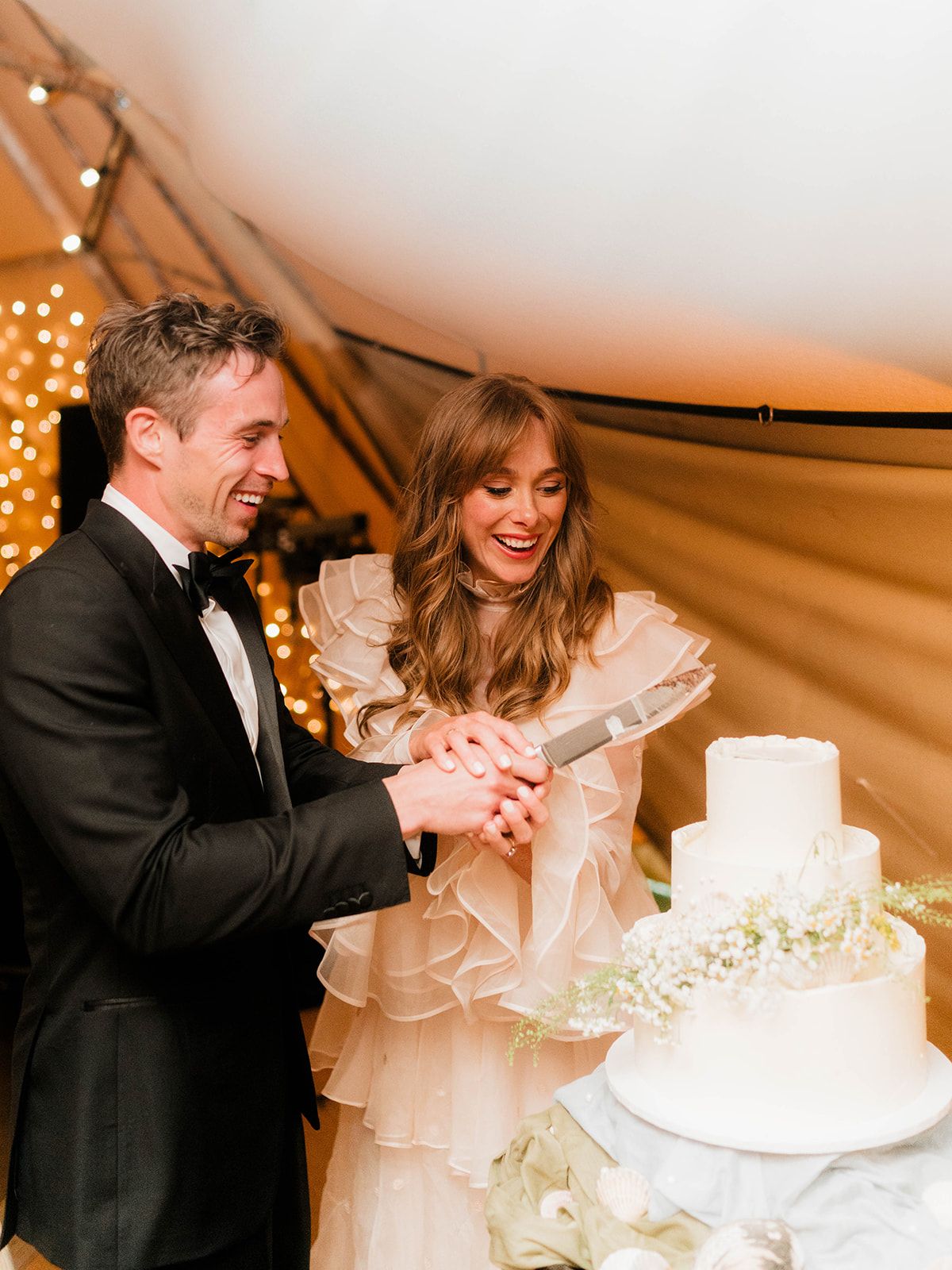 Newlyweds cut their elegant white tiered wedding cake decorated with baby's breath flowers.