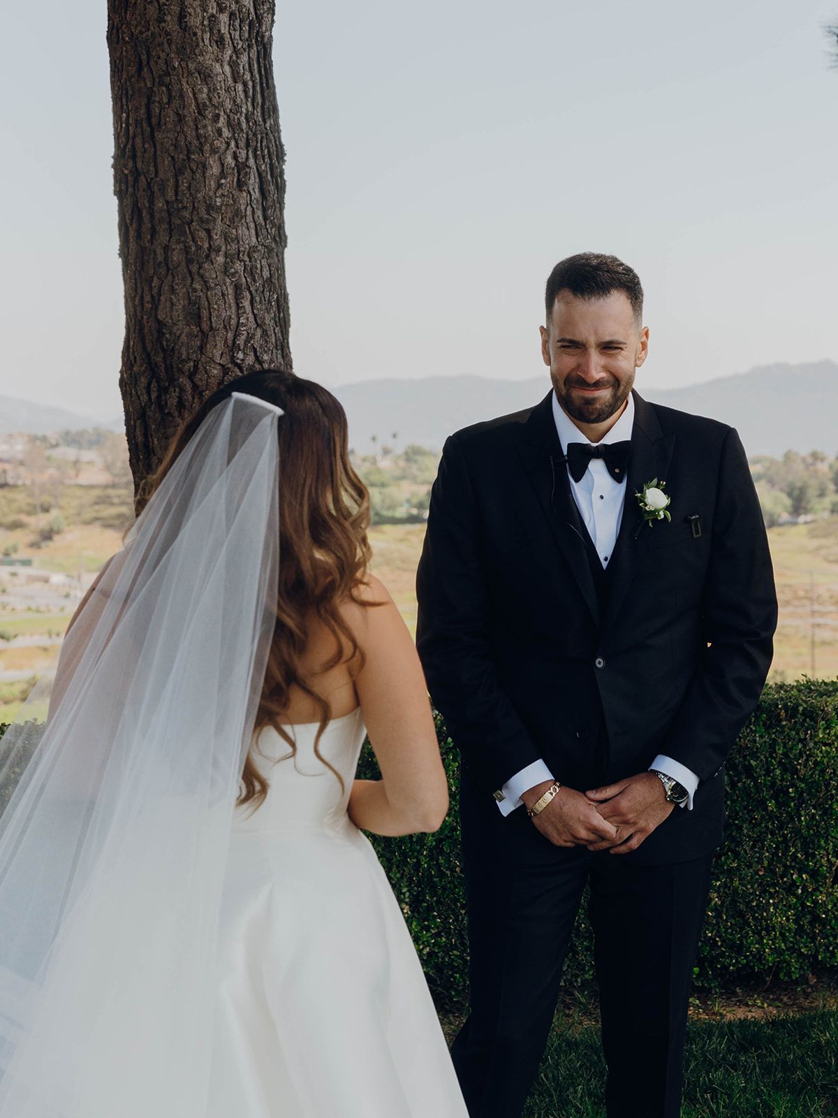 A wedding couple shares a first look moment under a tree with scenic mountain views in the background.