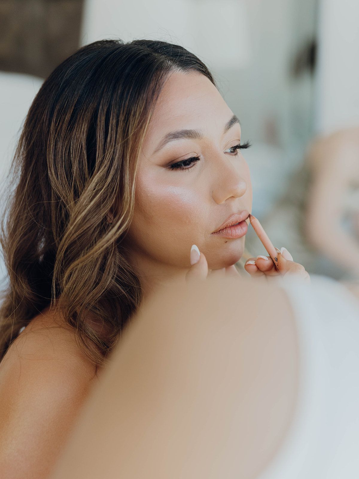 Professional makeup artist applying lip color during a bridal beauty preparation session with soft natural lighting.
