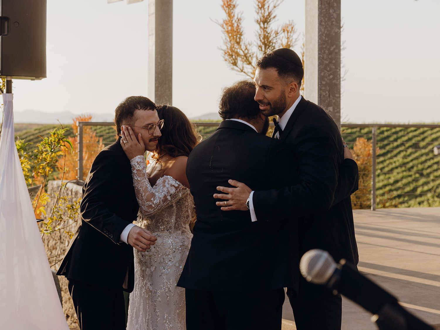 A wedding celebration unfolds on a scenic patio overlooking rolling vineyard hills at sunset.