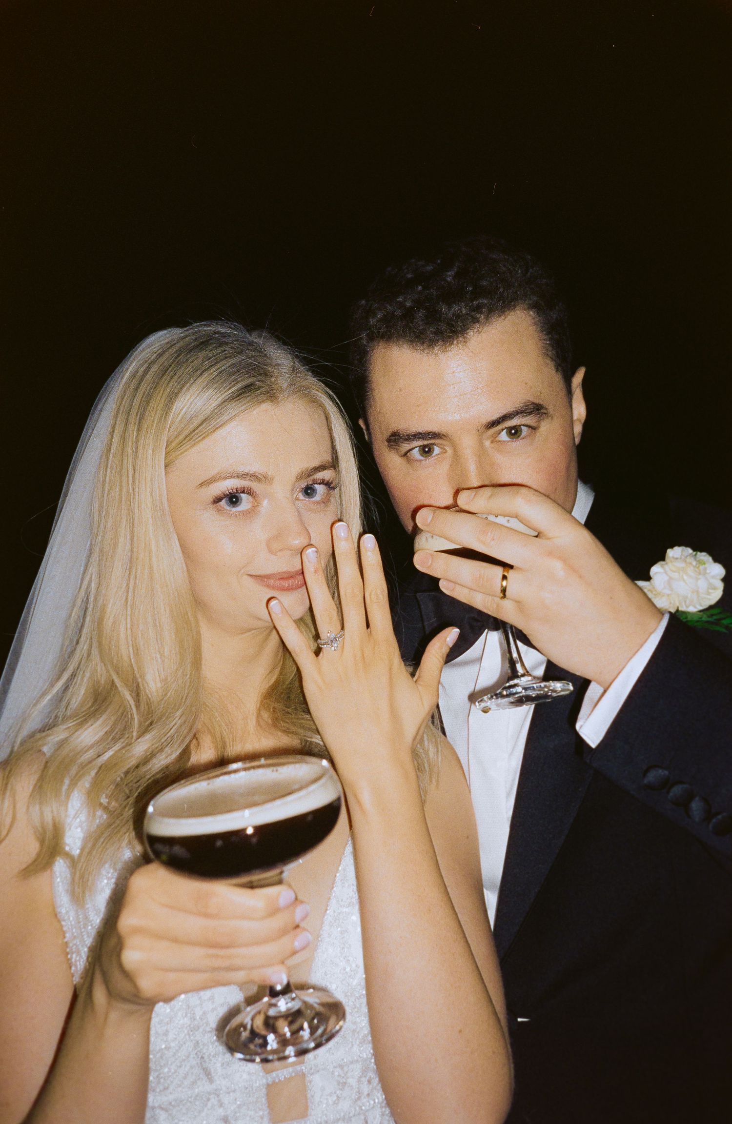 A large photo showing a wedding couple in formal attire drinking an espresso martini holding their ring fingers up