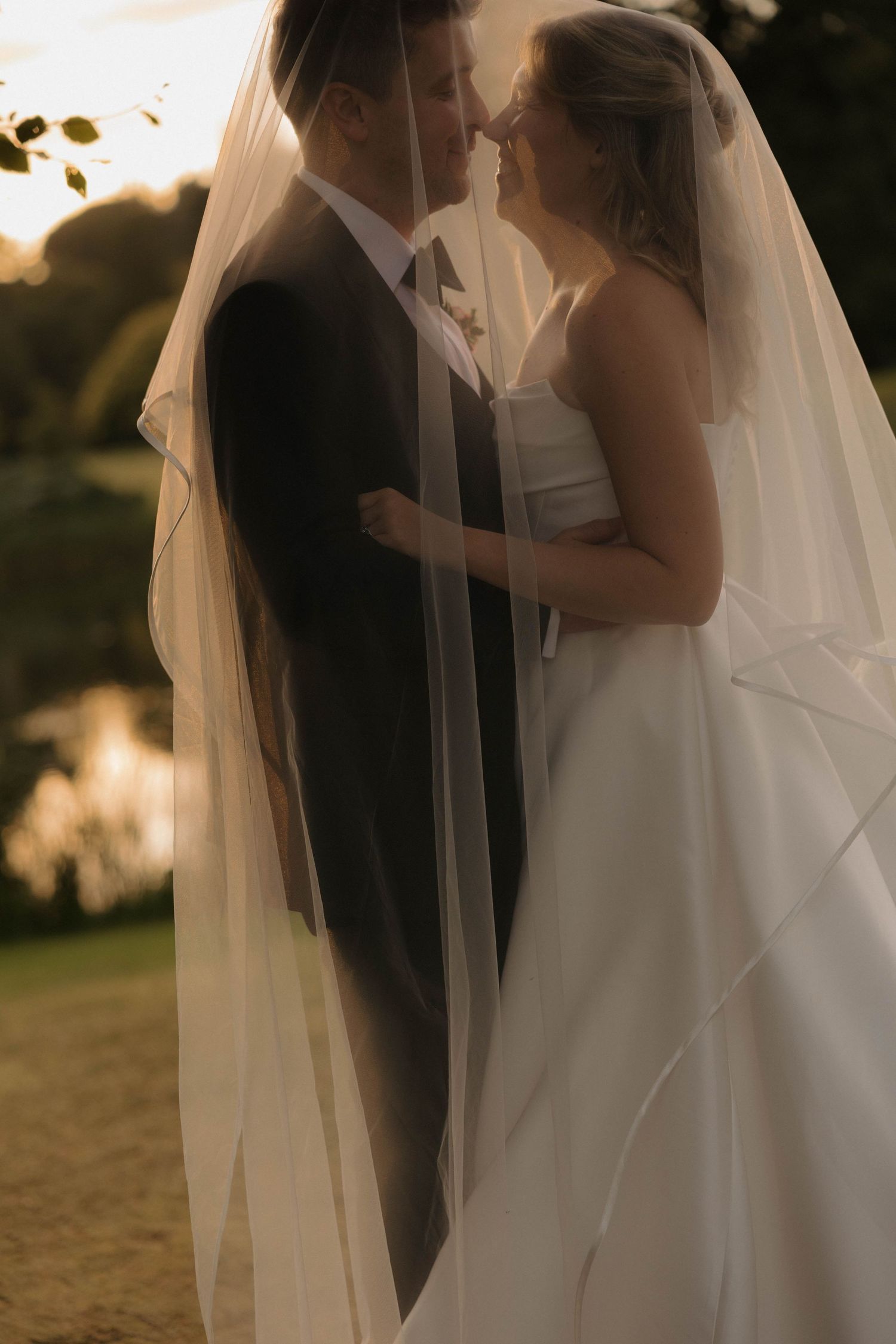 Romantic sunset silhouette of newlyweds sharing an intimate moment under a flowing veil.