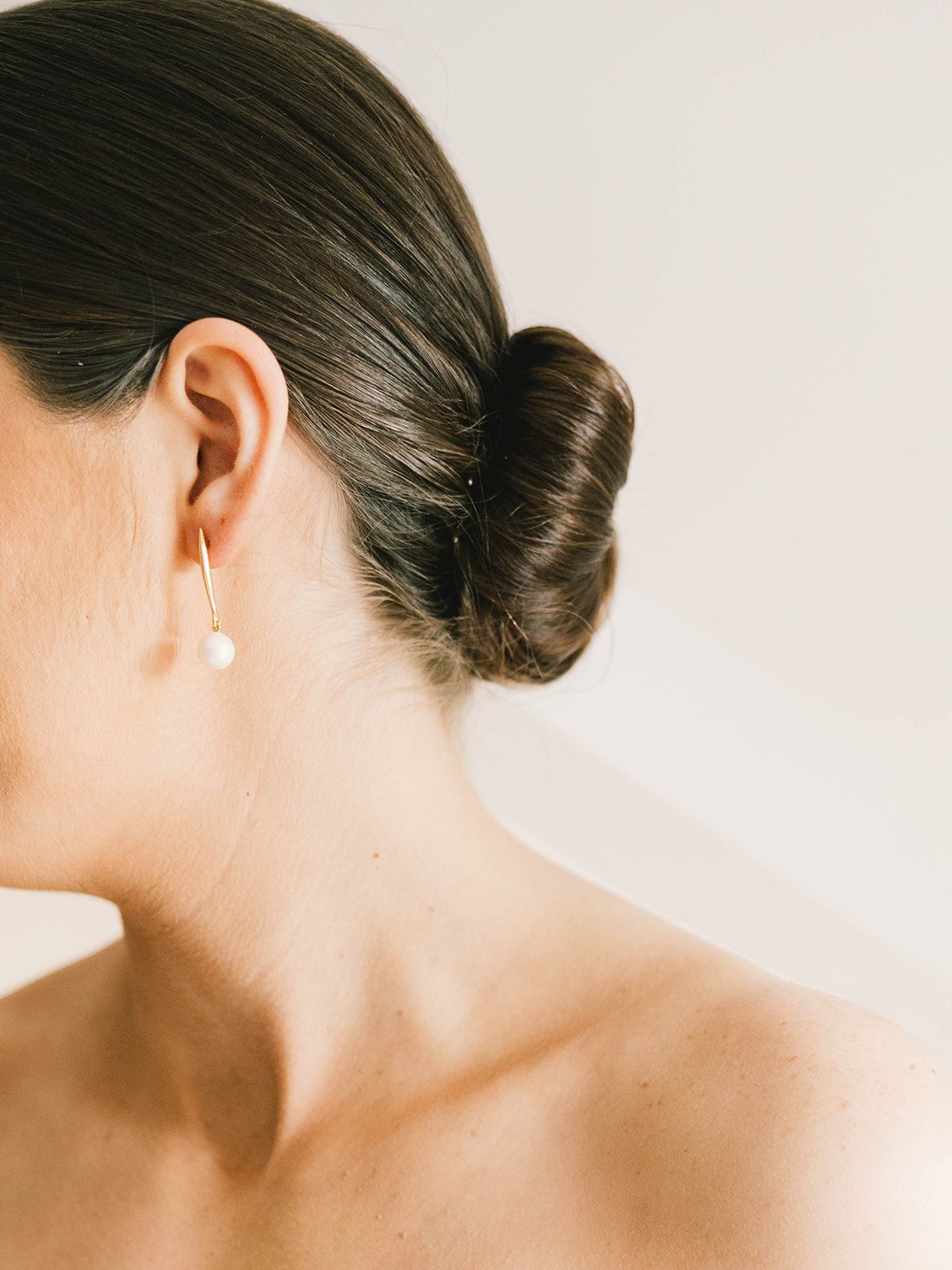 Sleek low bun hairstyle with a pearl drop earring against a light backdrop.