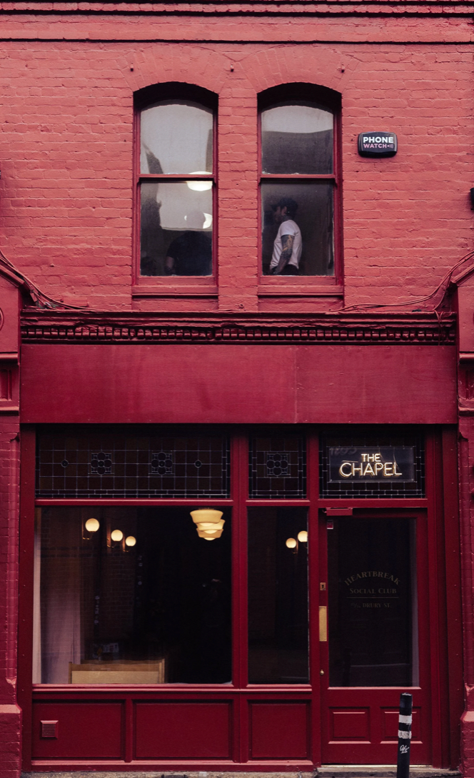 A red brick storefront with 'The Chapel' signage and vintage-style windows and lighting fixtures on a historic building.