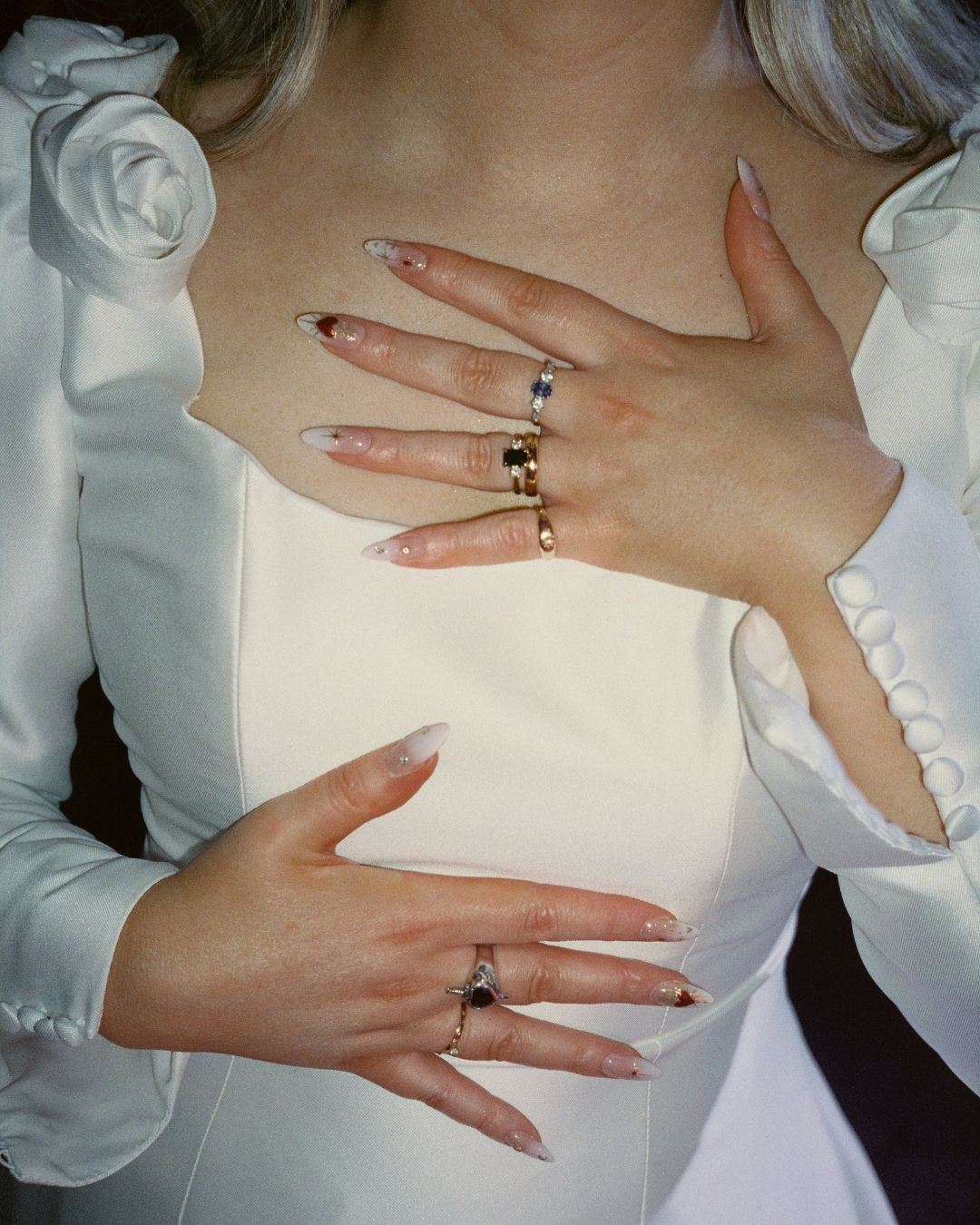 Close-up of hands wearing multiple silver rings against a white dress with ruffled long sleeves.