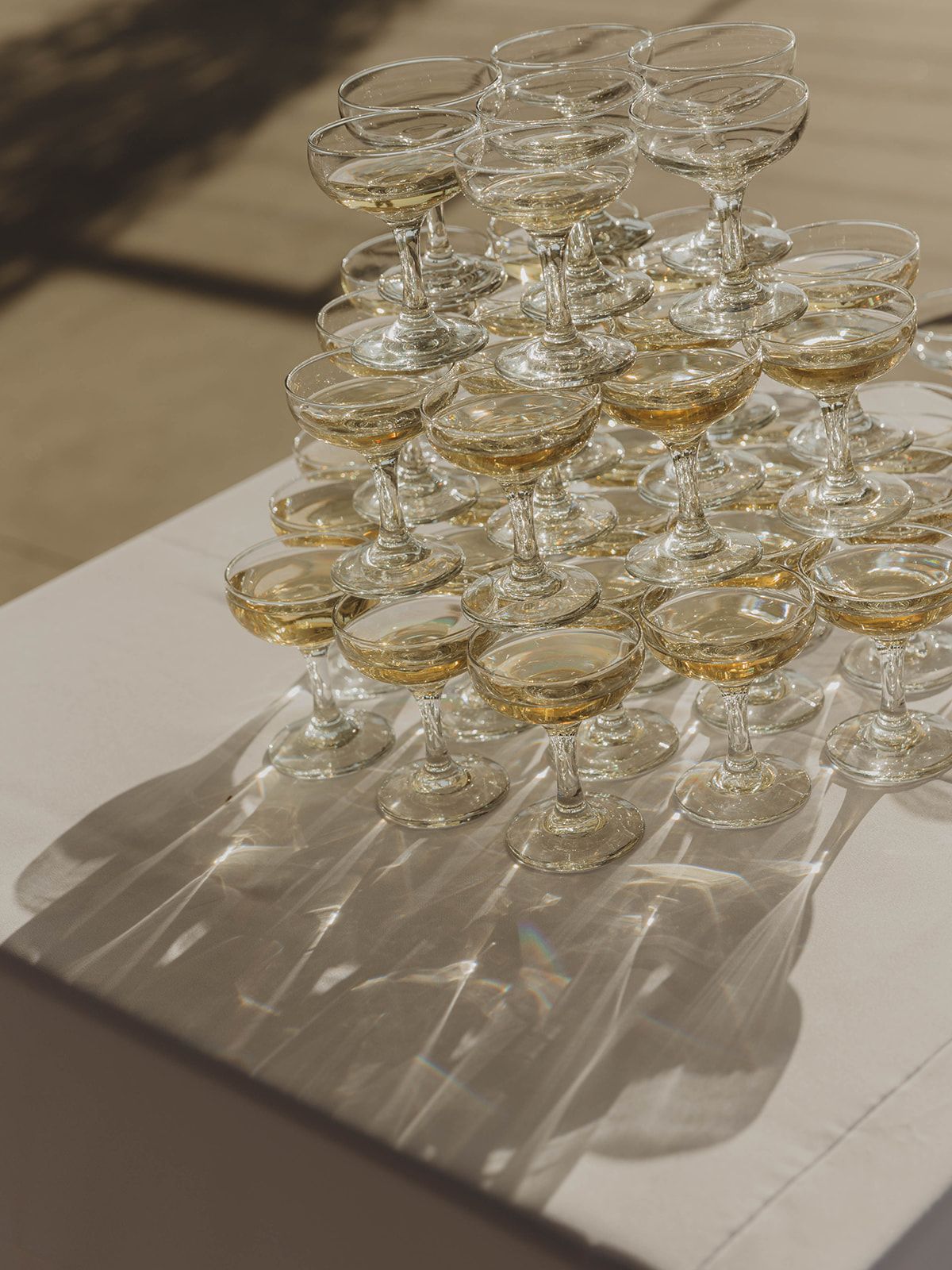 Elegant champagne coupe glasses arranged in pyramid formation cast dramatic shadows against a light surface.