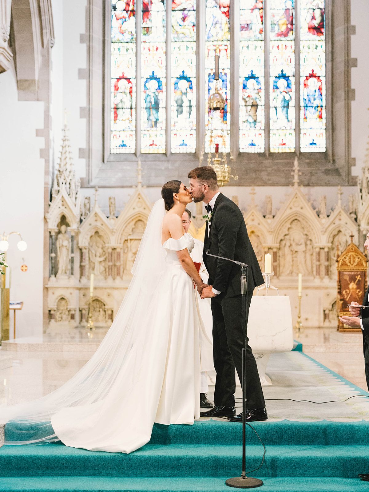 A romantic wedding ceremony moment in a church with stained glass windows and turquoise carpeted altar.