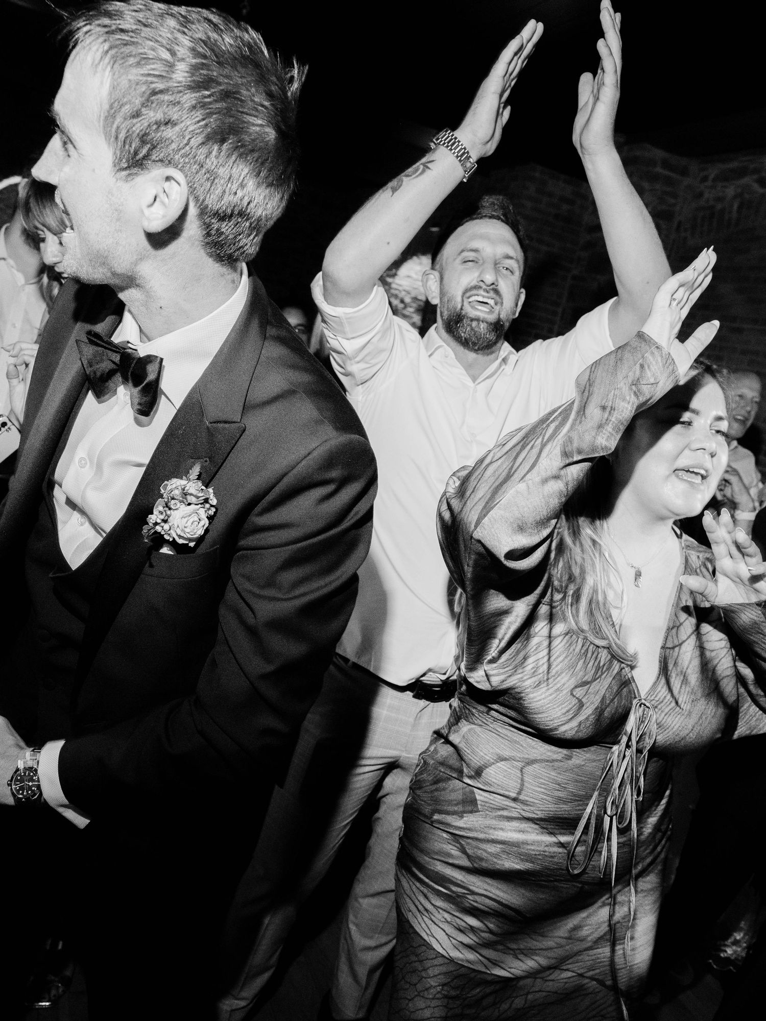 Black and white photo of wedding guests dancing energetically at a reception celebration.