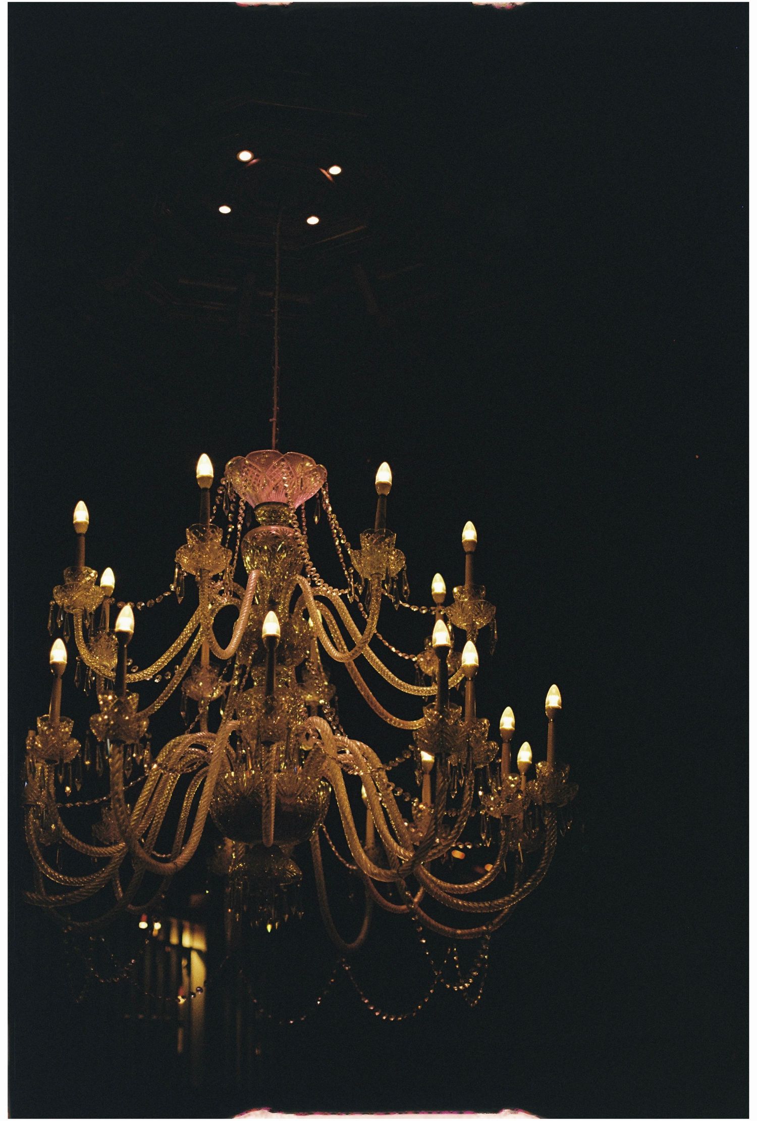 Elegant crystal chandelier with candle-style lights glowing warmly against a dark background.