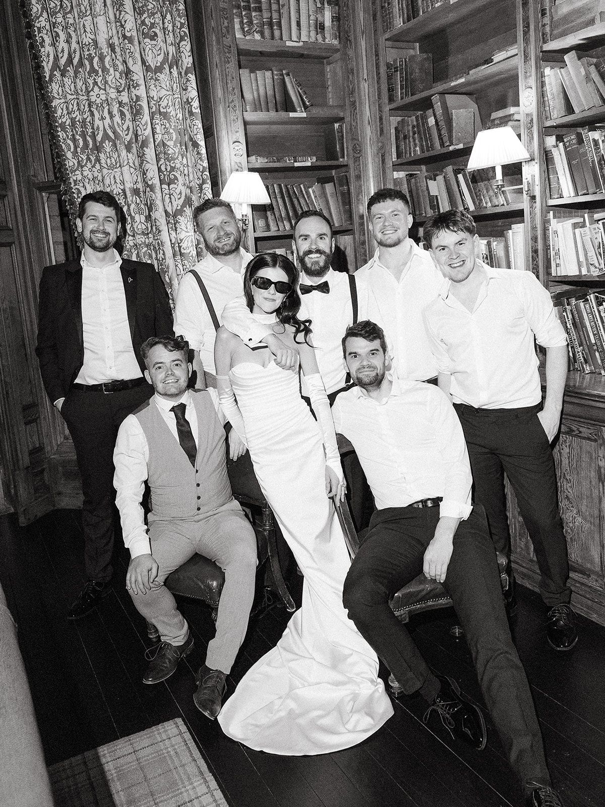 Four black and white photos show wedding party members dancing and celebrating in a library setting.