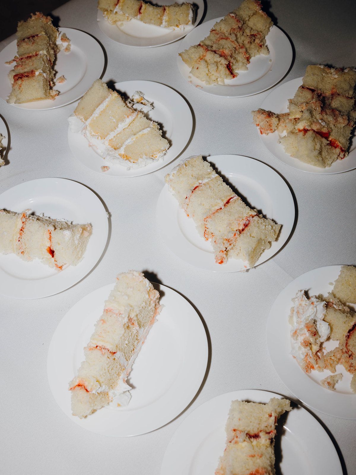 Multiple slices of white layered sandwiches with thin red filling arranged on white plates against a dark background.