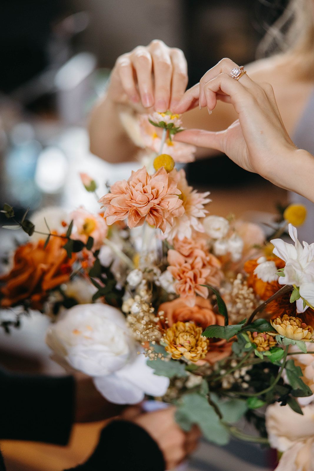 Hands arranging a beautiful bouquet of peach, orange and white flowers with delicate greenery and baby's breath.