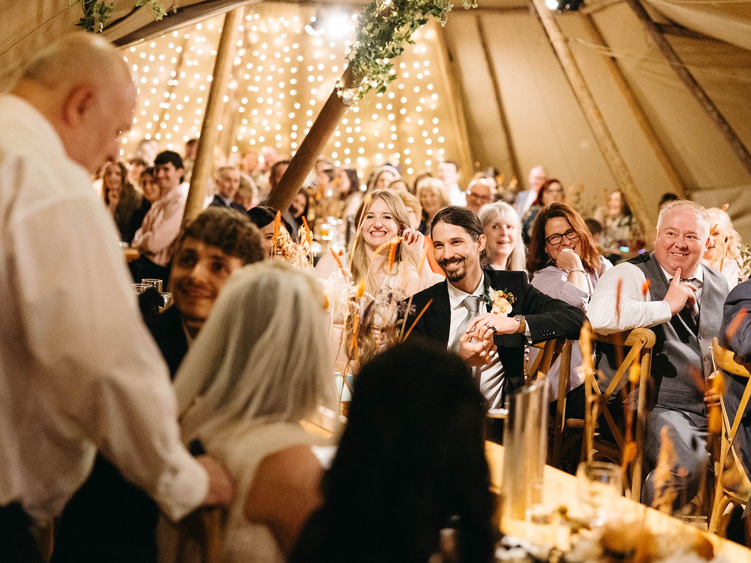Joyful wedding celebration inside a beautifully lit tipi tent with guests cheering during a daytime ceremony.