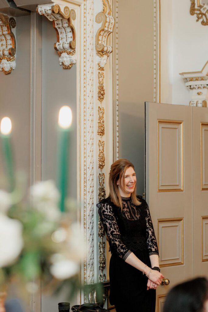 Someone in a black lace dress stands in an elegant room with ornate gold trim and moldings.