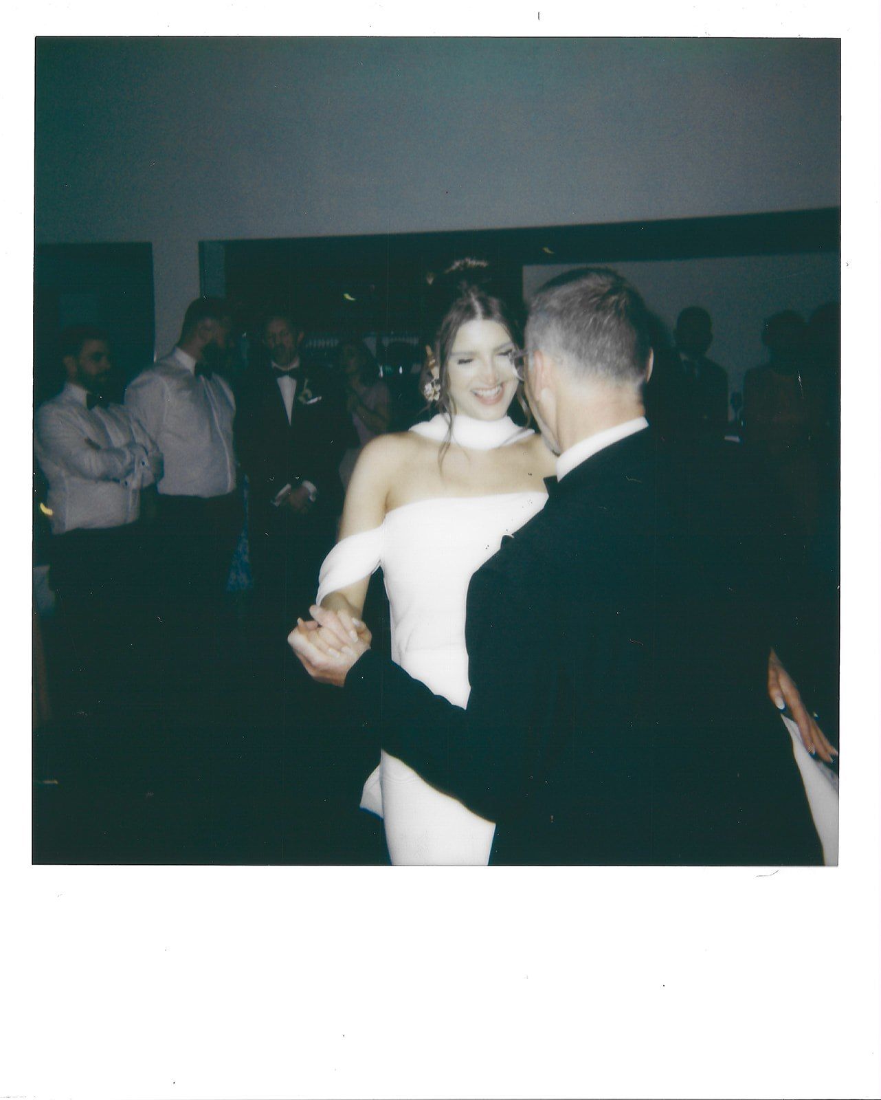 Couples dancing together in a dimly lit room during what appears to be a wedding reception or formal event.