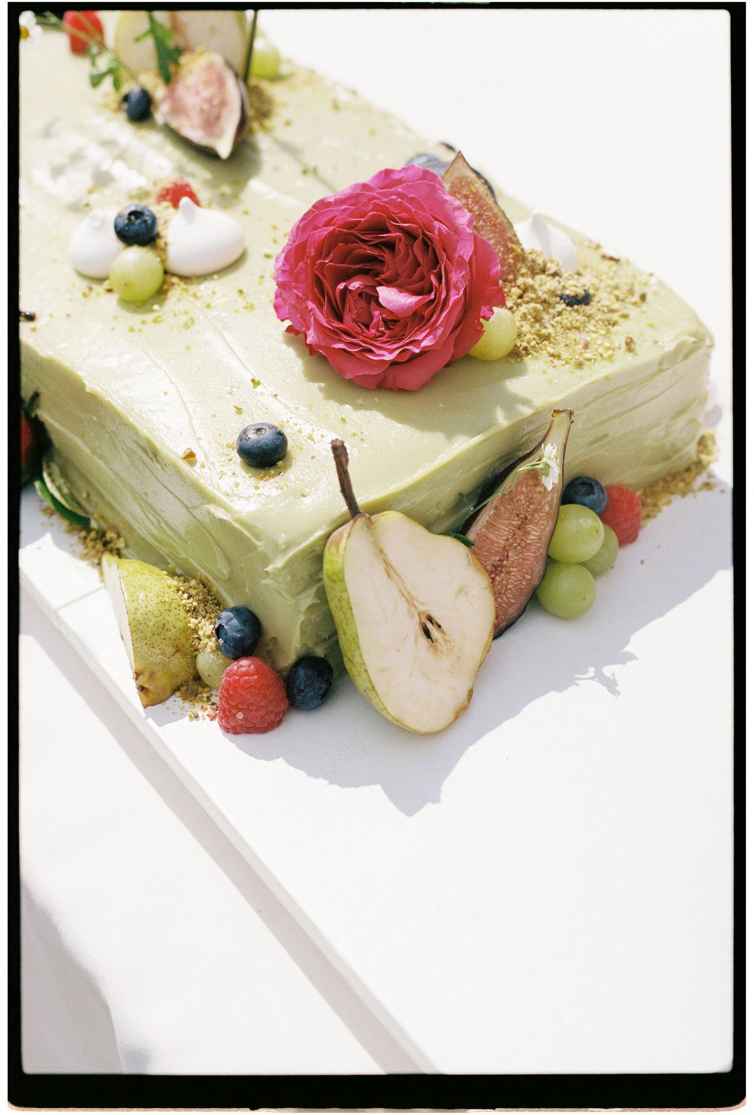 Elegant green wedding cake decorated with fresh pear, blueberries, roses and fruit toppings.